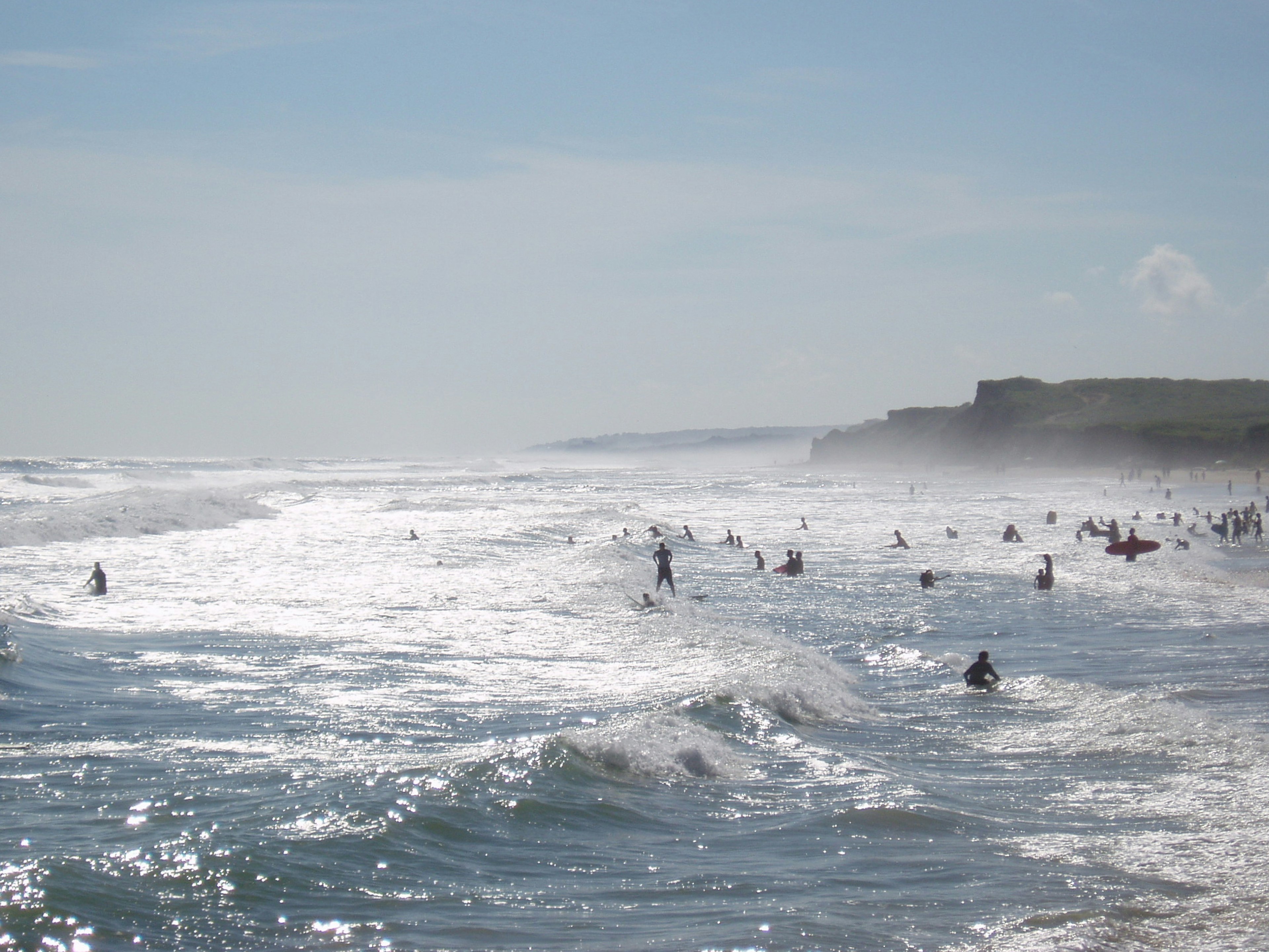 Surfers silhouetted against the sun wait in the sea hoping to catch a wave