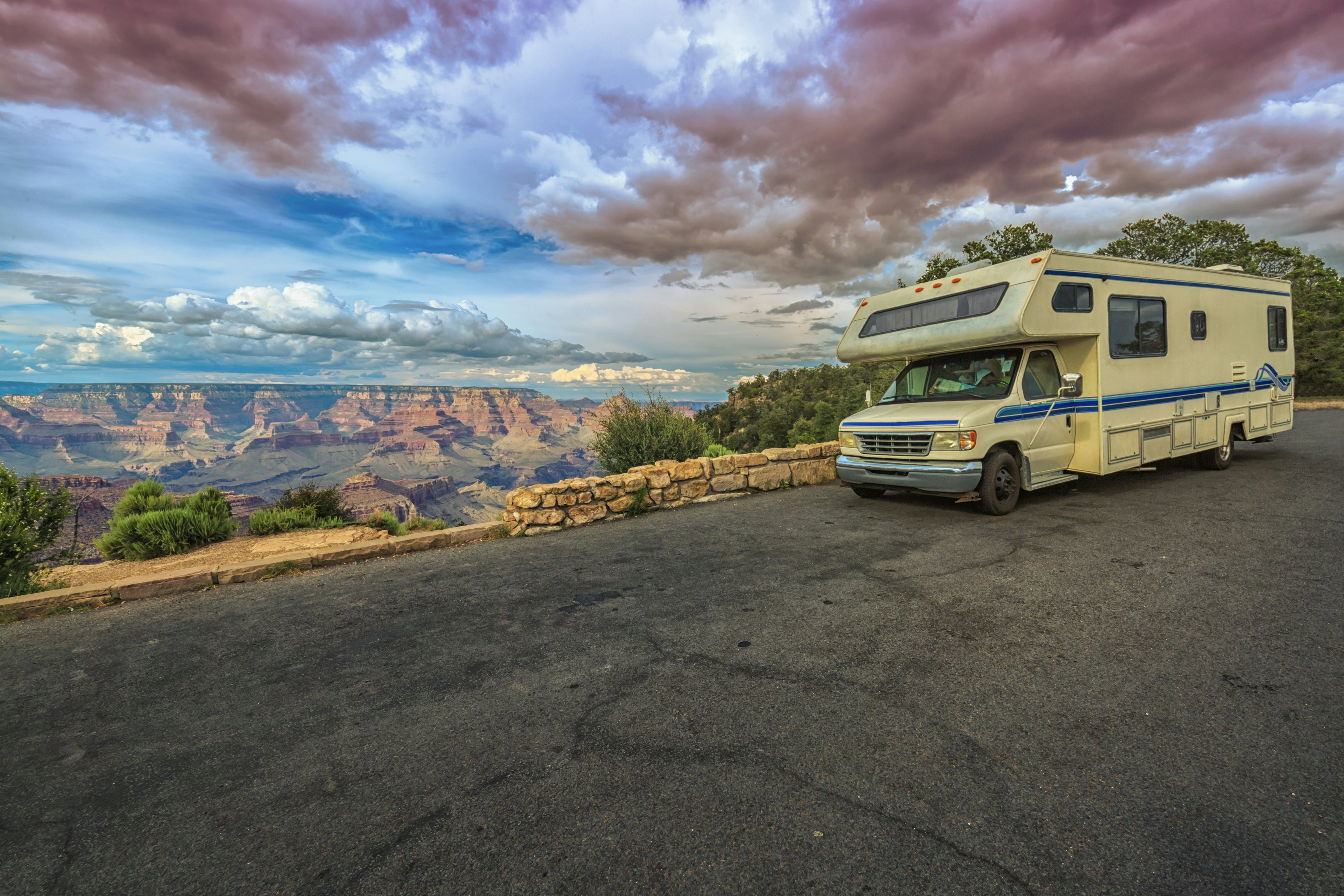 A large camper van parked near a large canyon valley with striped rocks at sunset.