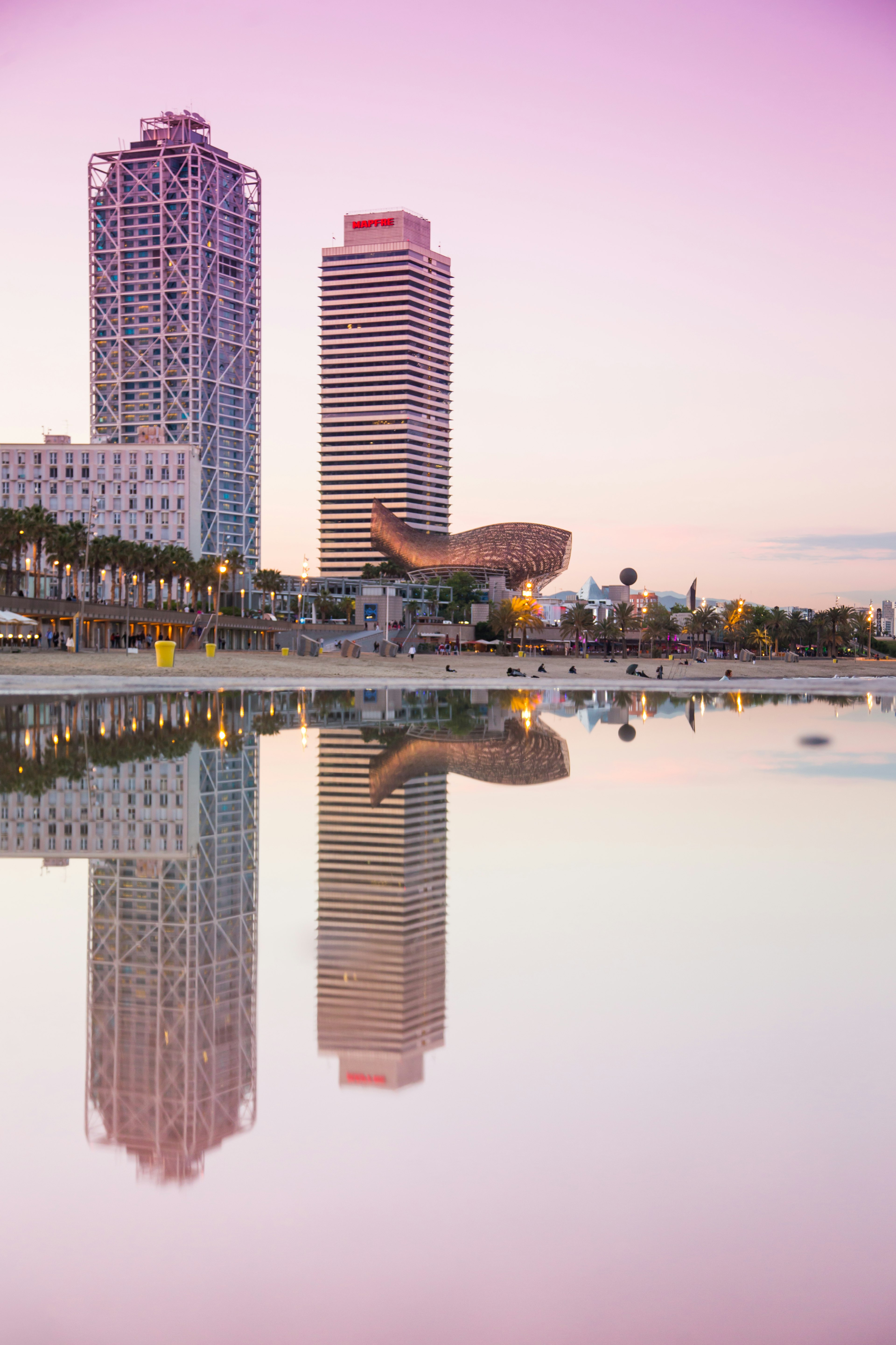 Frank Gehry’s El Peix (Golden Fish) sculpture dangles above the quiet sands of Somorrostro Beach in Barcelona during a pink sunset