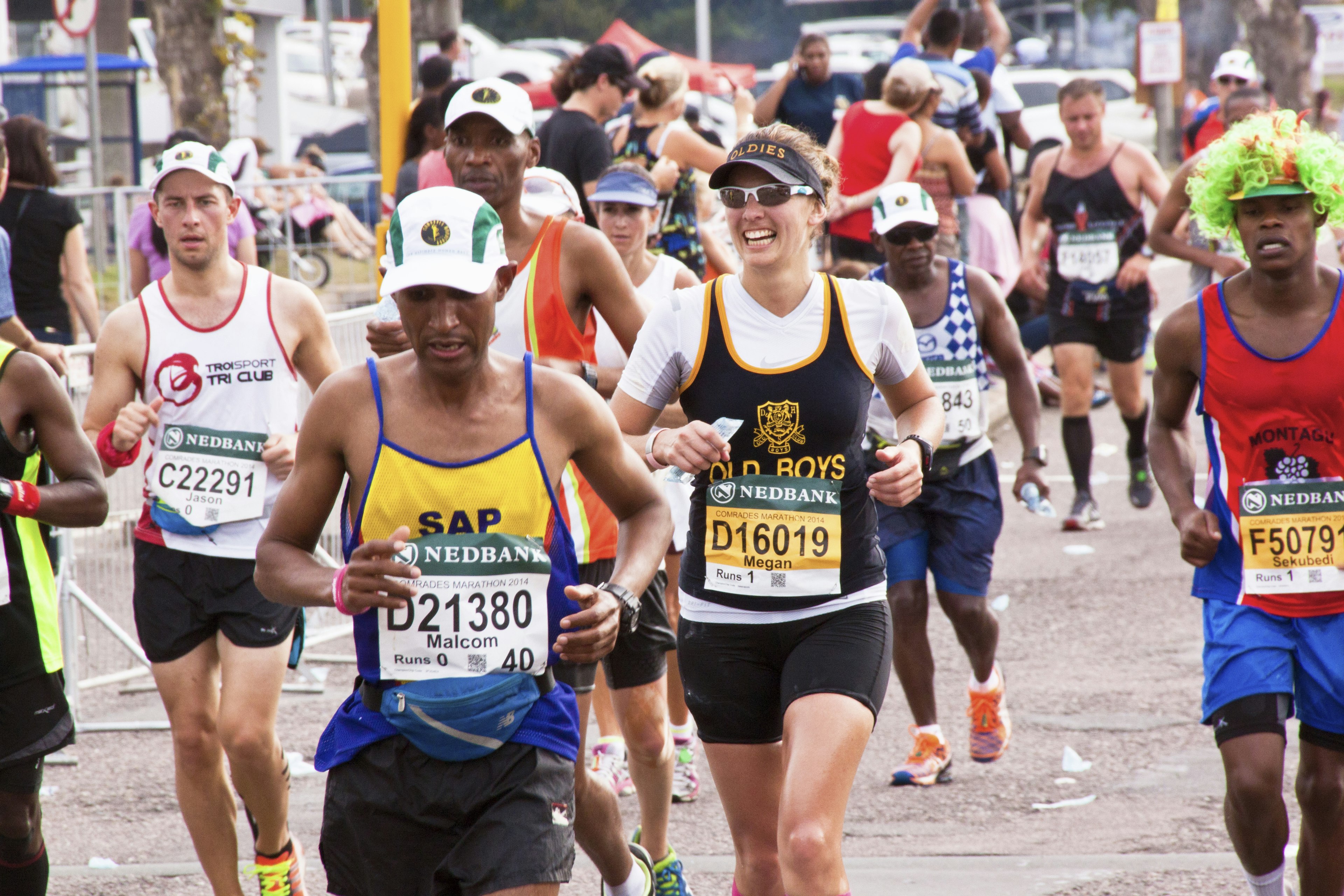 A group of competitors wearing numbered bibs run along a stretch of road in an ultra marathon