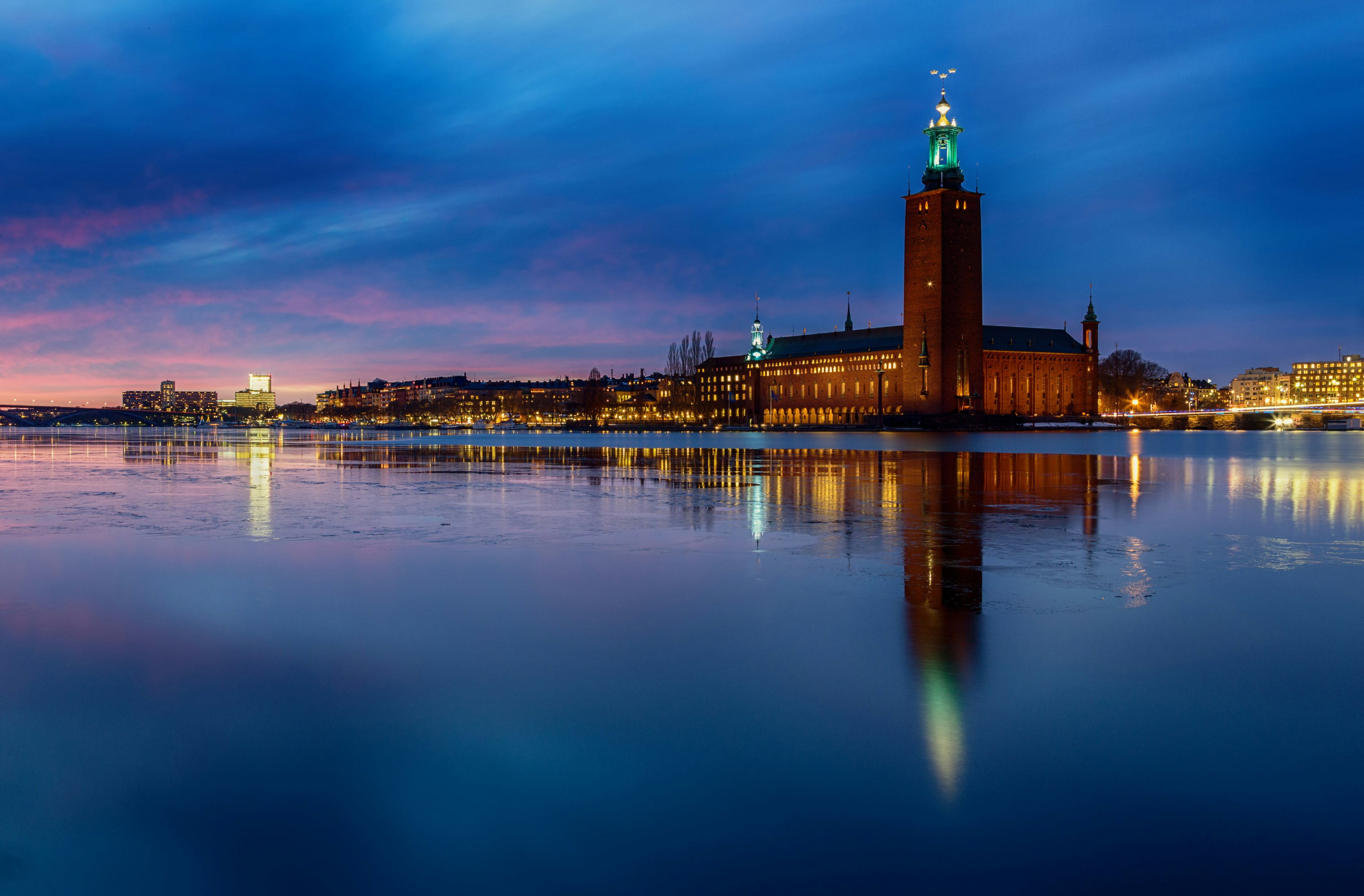 The red-brick tower of Stadshuset (City Hall) is reflected in the harbor water at sunset, Stockholm