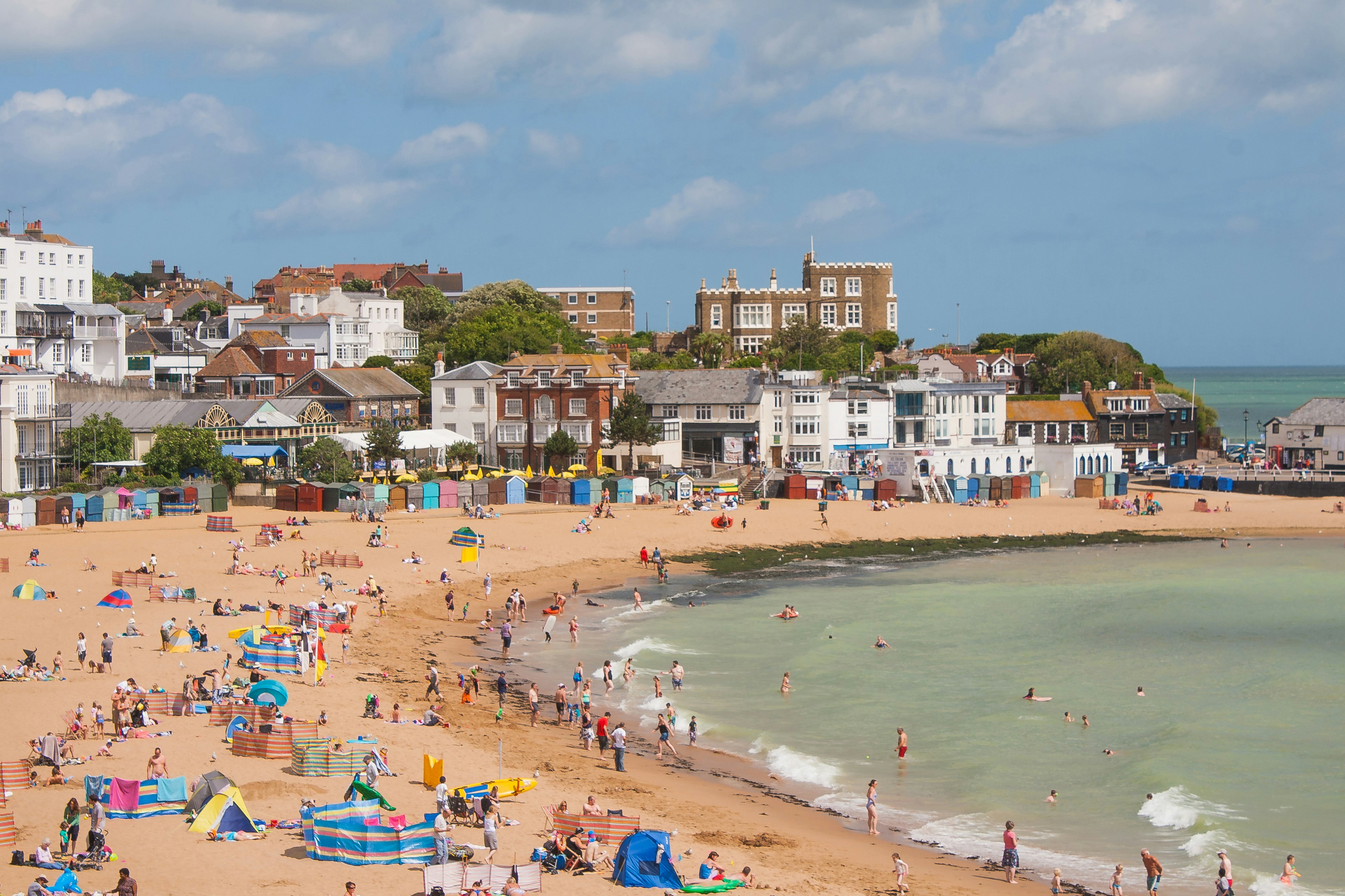 A busy sandy cover with lots of groups of people enjoying a sunny day by the beach