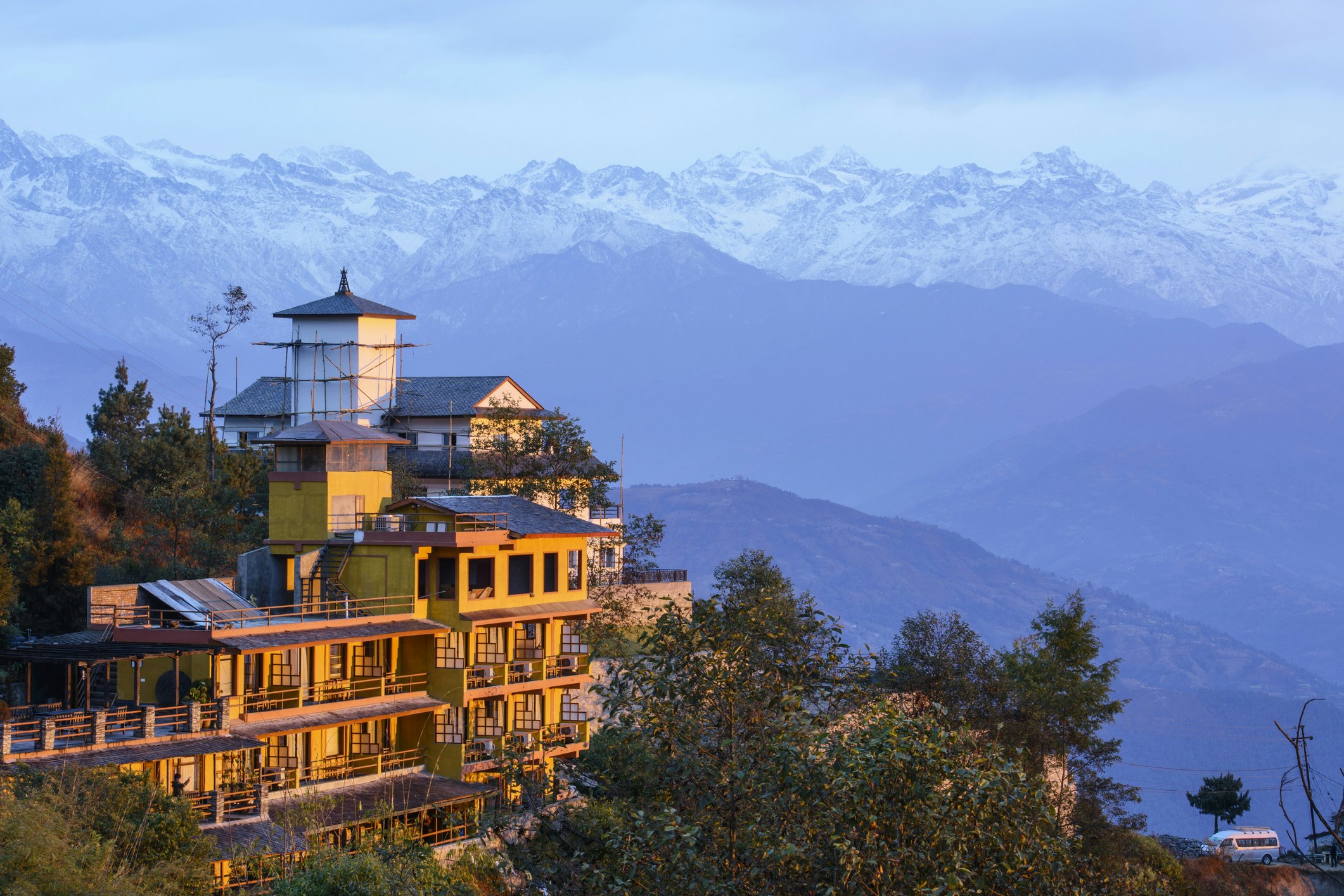 A hilltop building glowing in the sunshine. In the distance is a snow-capped mountain range.