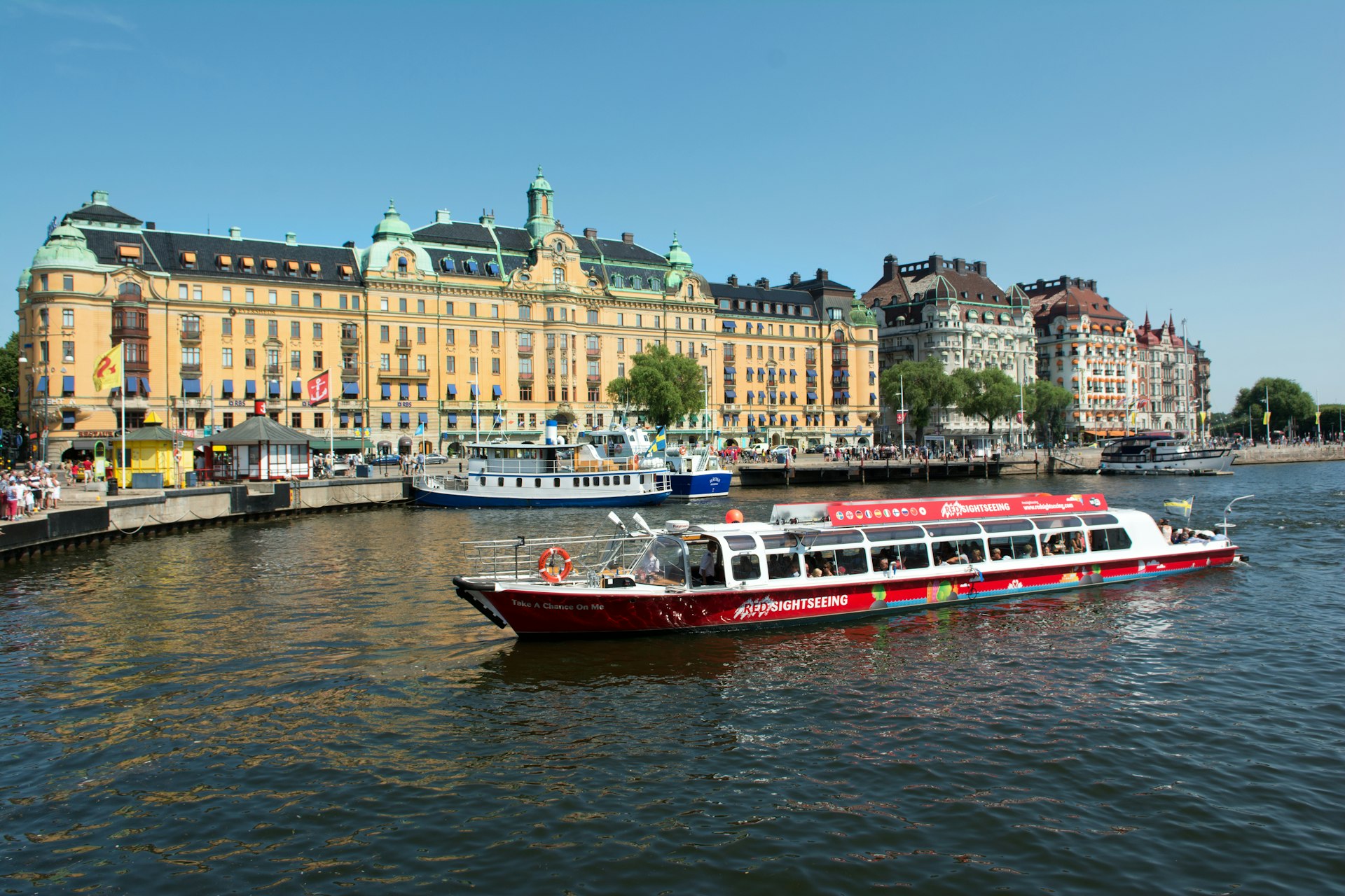 A red sightseeing boat passes the Grand Hotel in Nybroviken, Stockholm, Sweden