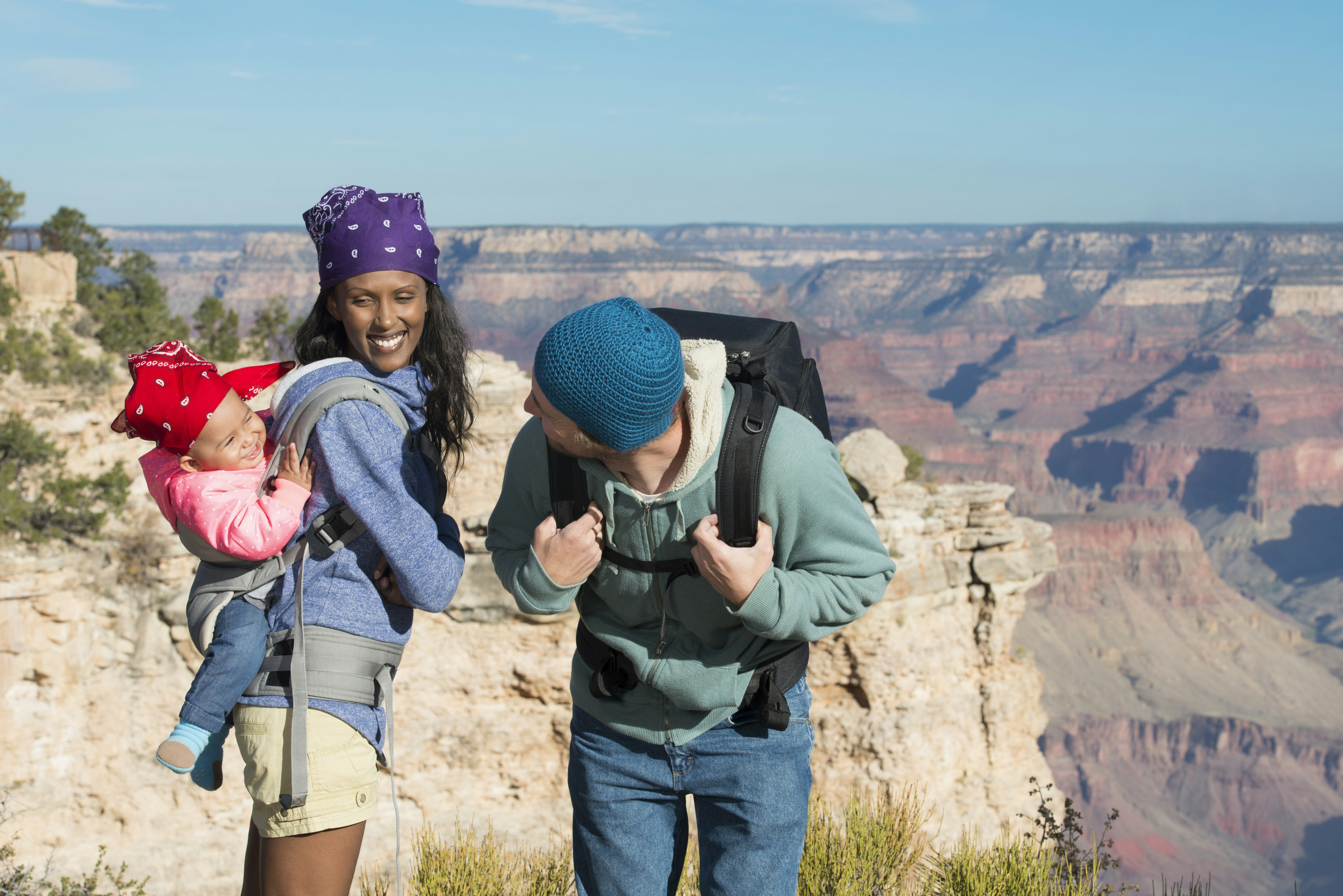 Young mixed-race family hiking at the Grand Canyon, the mother carrying their baby in a carrier on her back and the father playing with her.