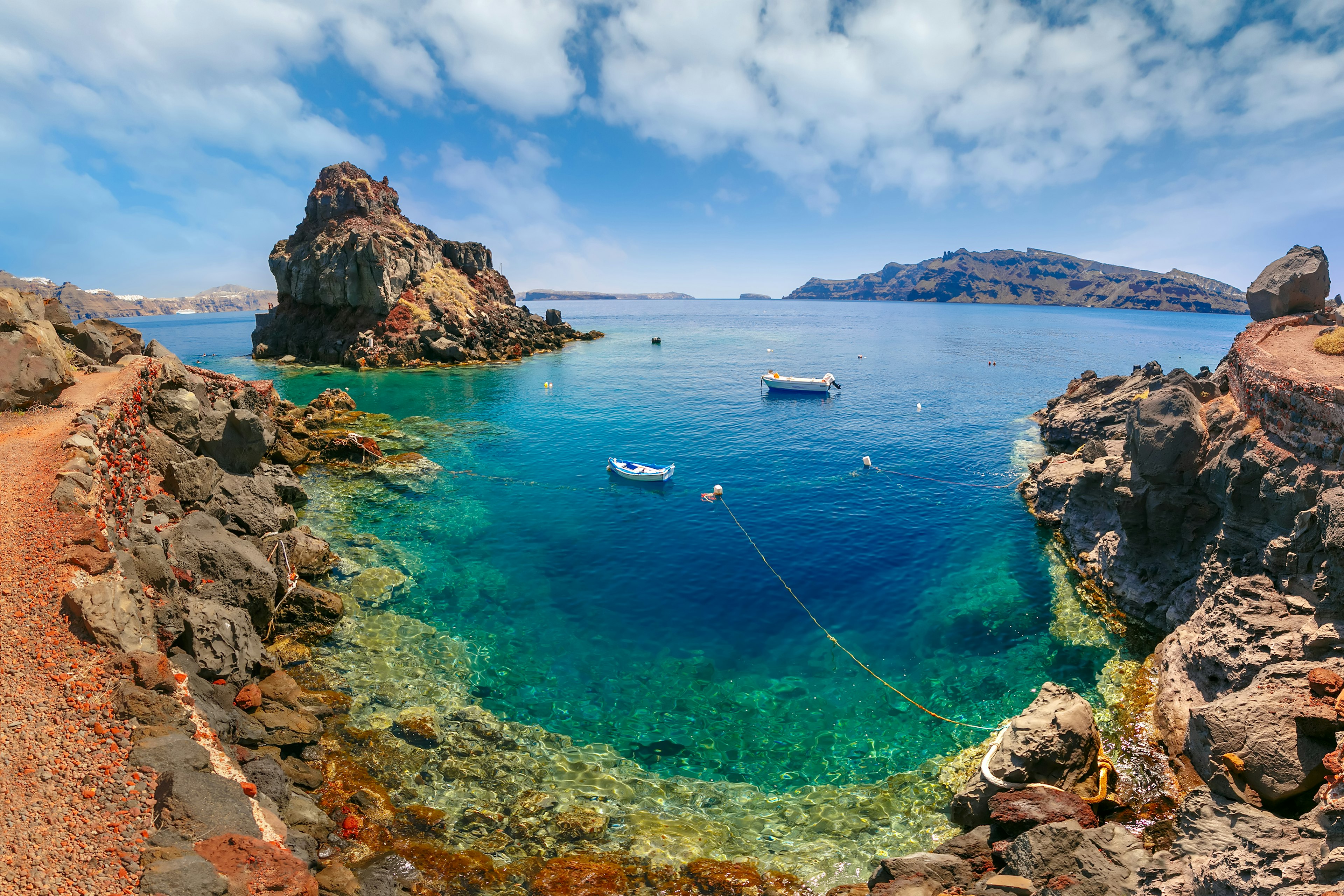 A cove where the red rocky shore meets bright and clear turquoise waters.