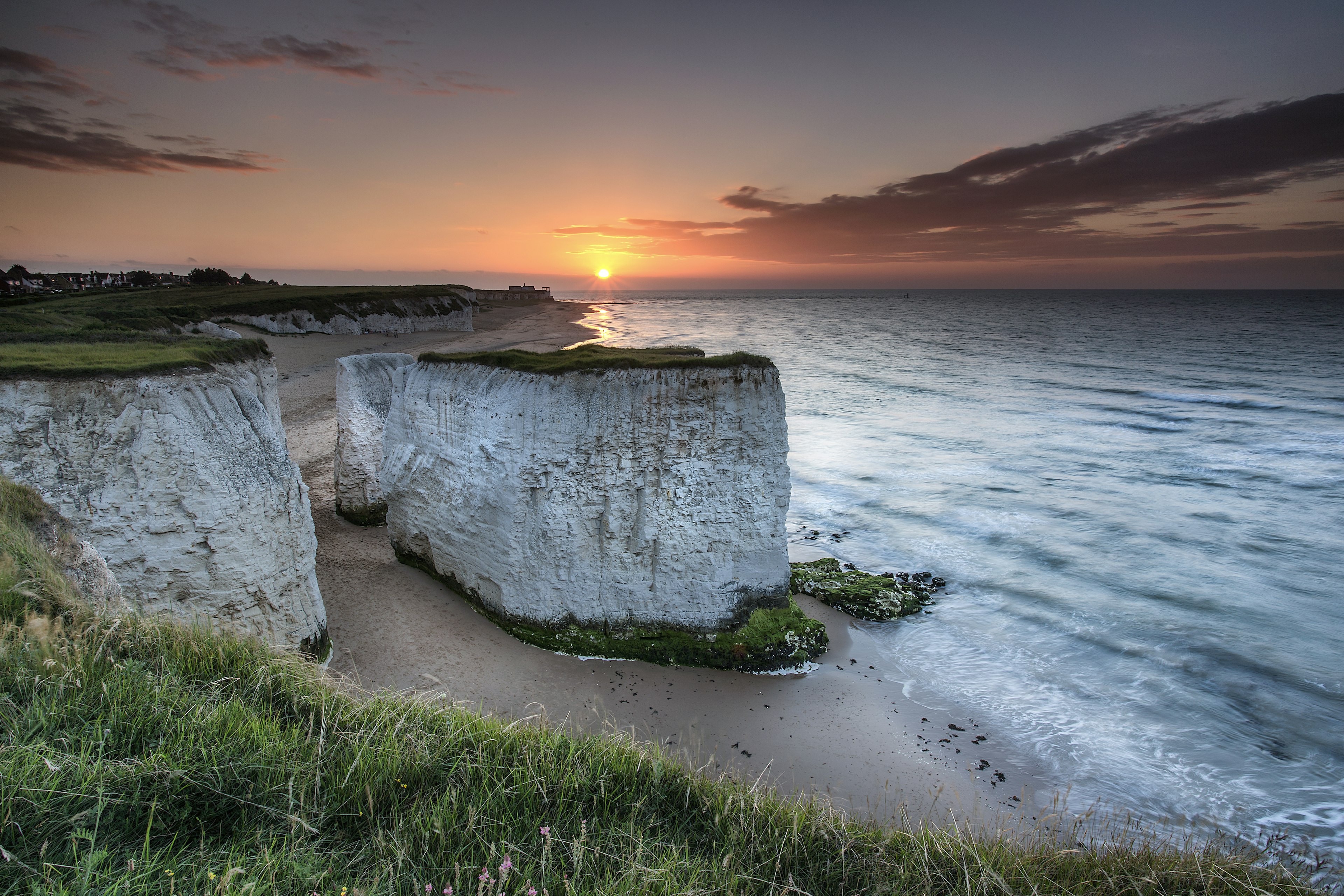 A low sun in the sky creating an orange glow over huge chalk stacks that stand on a sandy beach