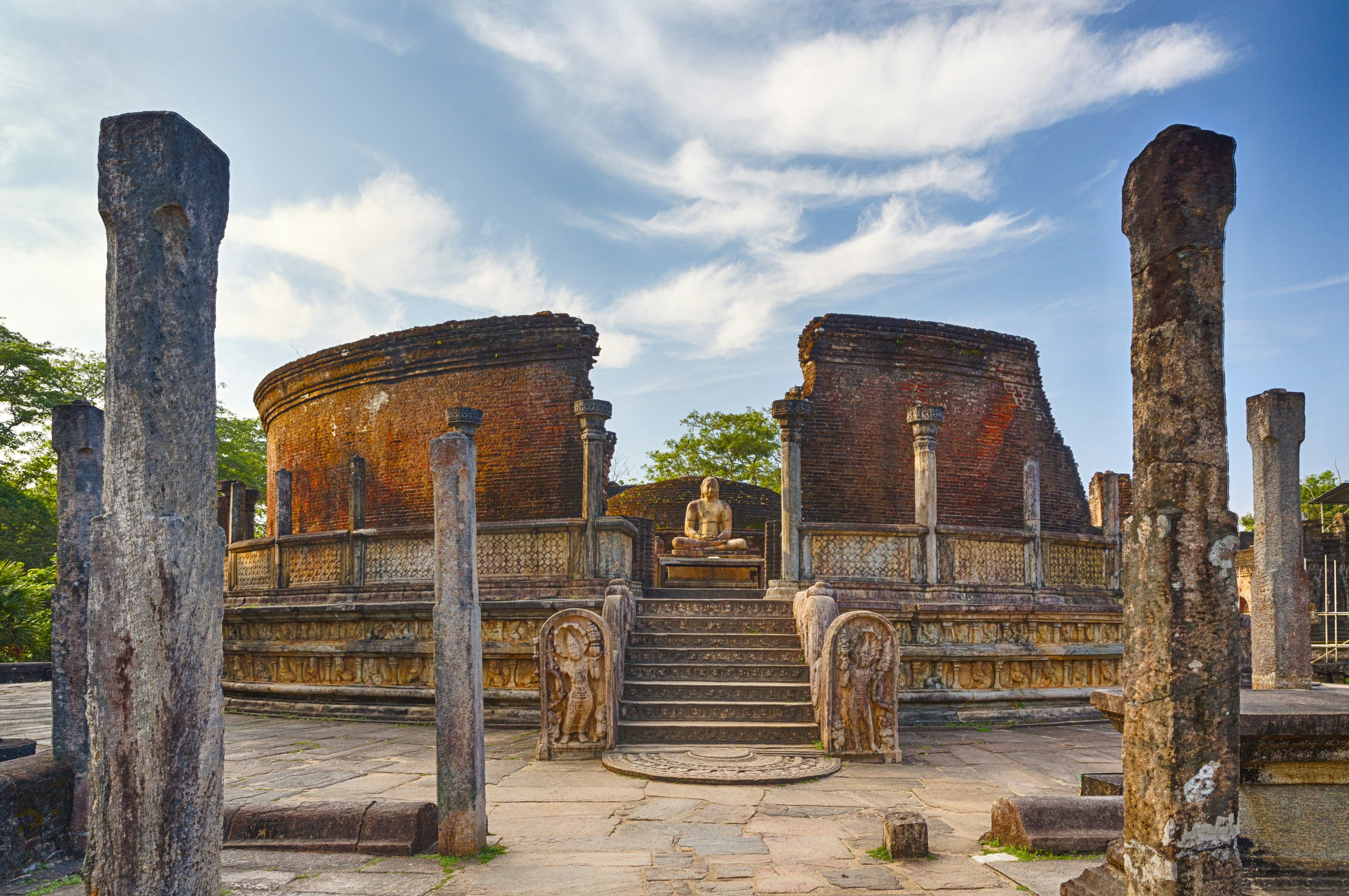 The crumbling brick walls and columns of a ruined temple with a buddha figure sat in the center