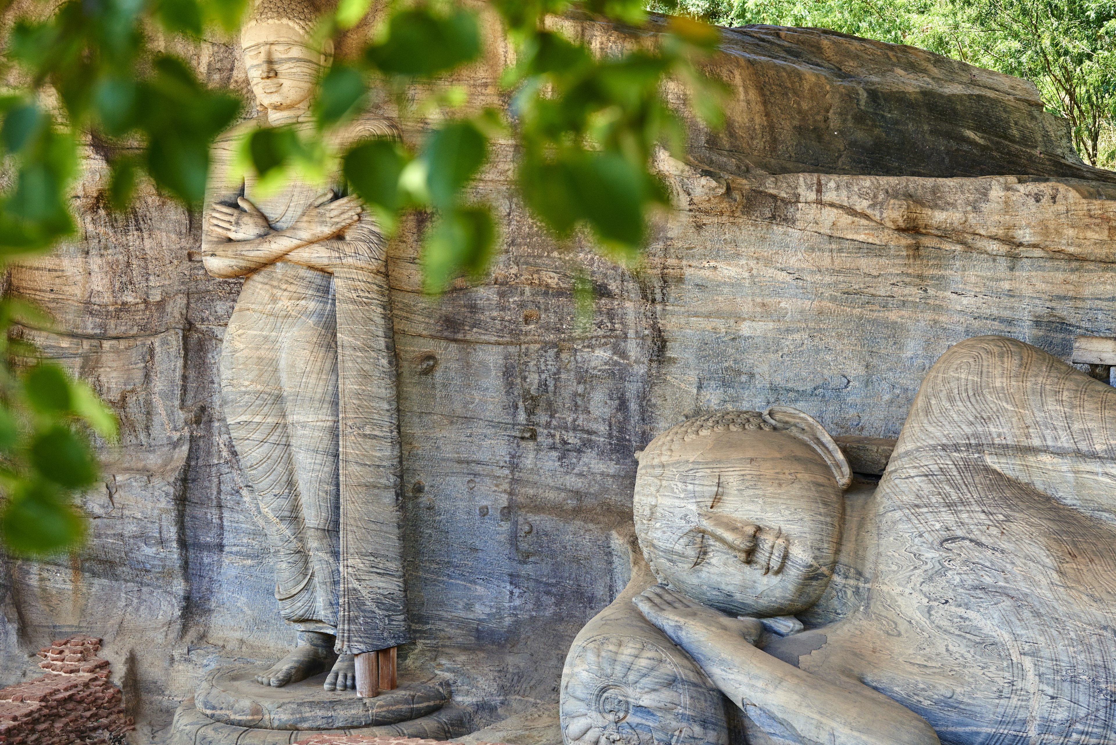 Monumental Buddha statues viewed through the leaves at the Gal Vihara temple complex, Polonnaruwa, Sri Lanka.