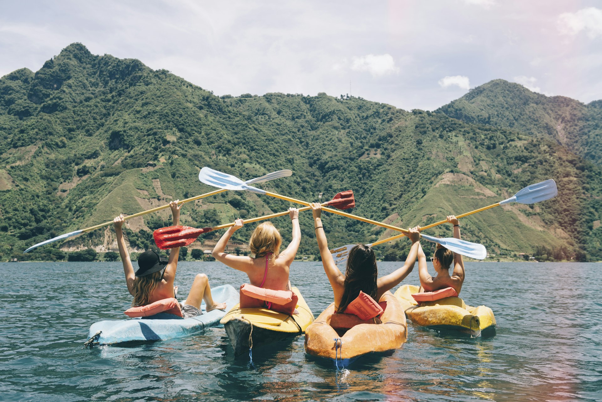 Rear view of four female friends celebrating in kayaks on Lake Atitlan, Guatemala.