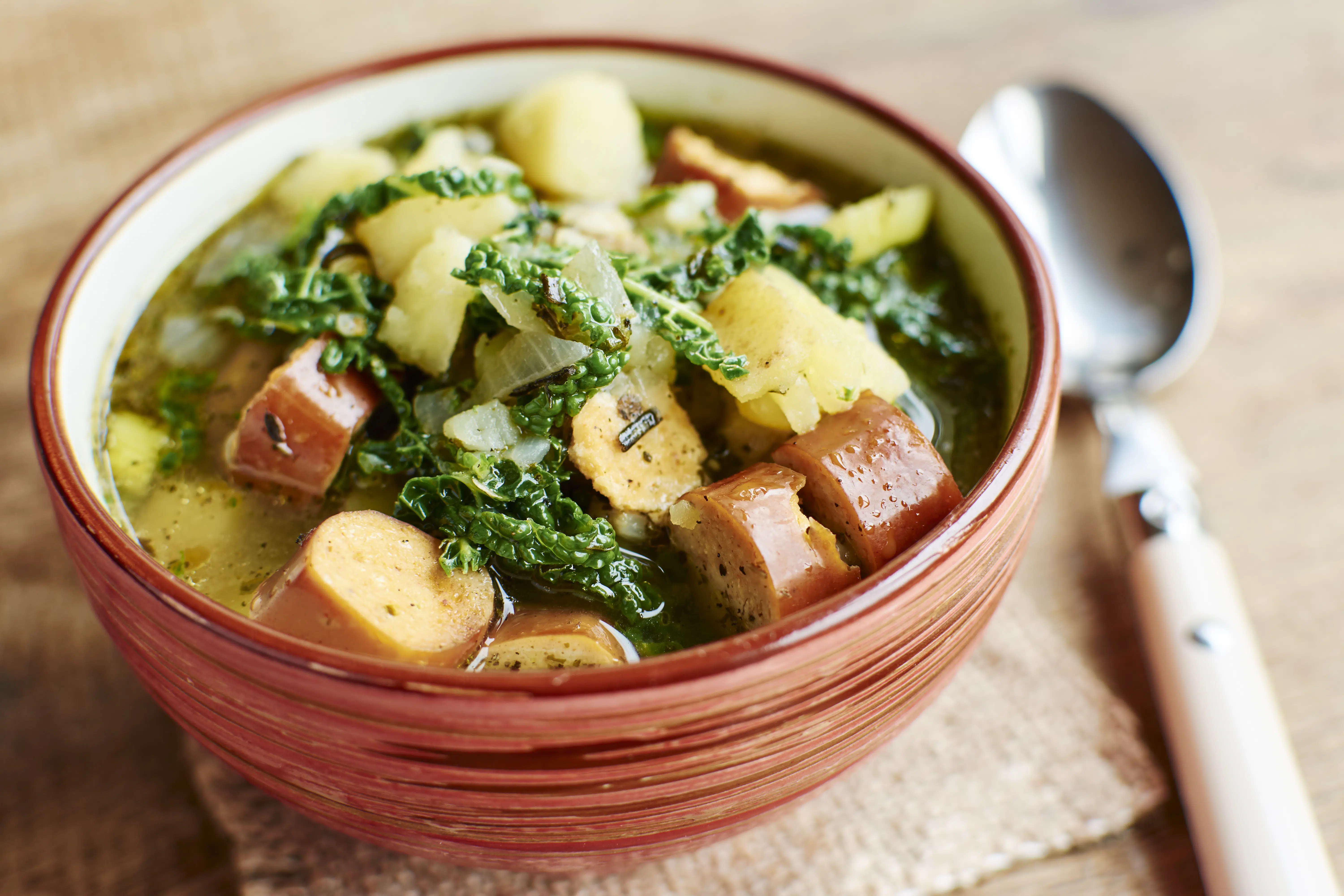 A terracotta bowl filled with sausage, kale and potato soup.