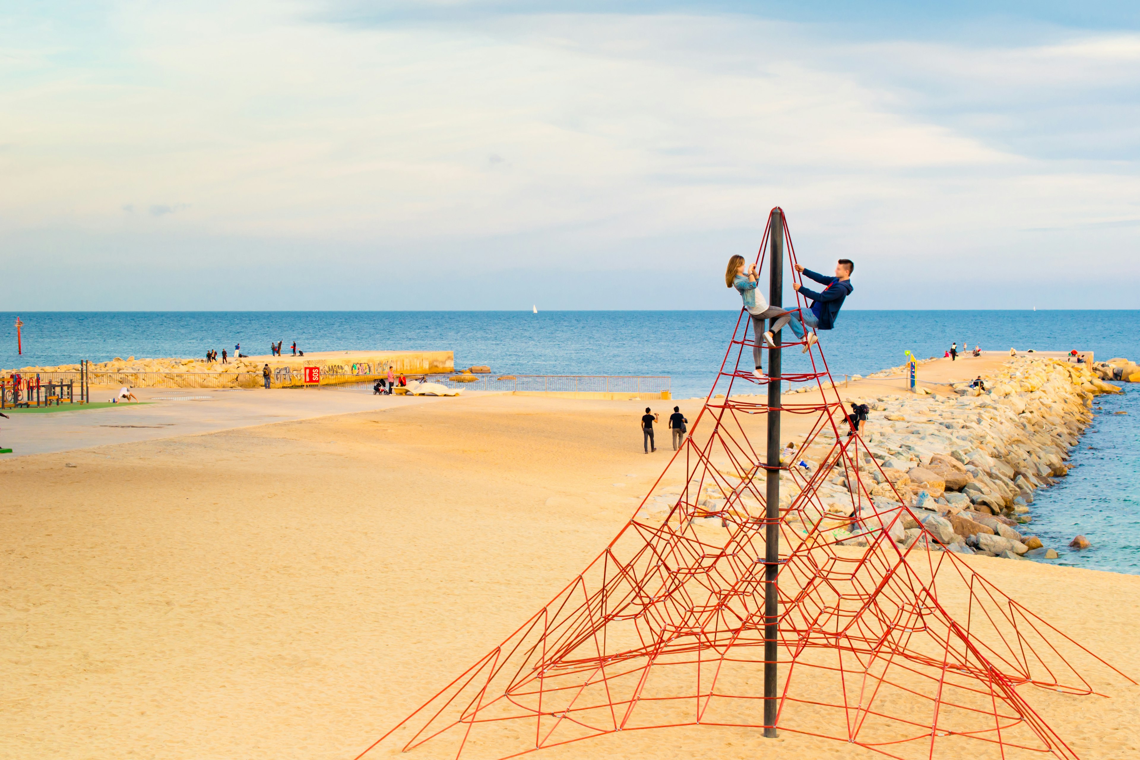 A man and woman clamber over a climbing frame at Nova Mar Bella Beach, Barcelona