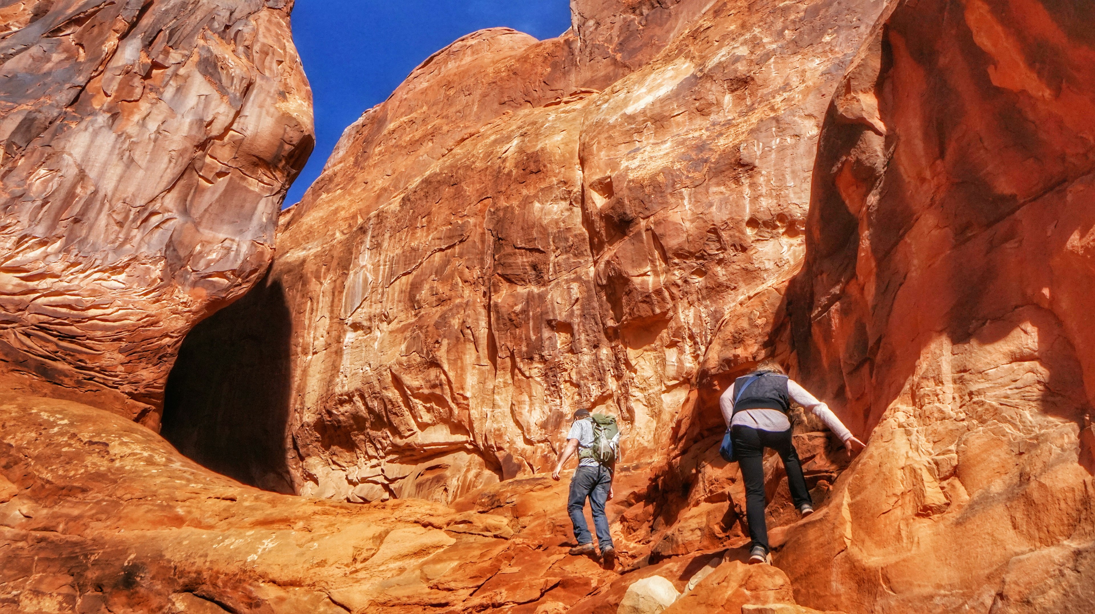 Два туриста поднимаются по камням на тропе Fiery Furnace в Национальном парке Арчес, Юта