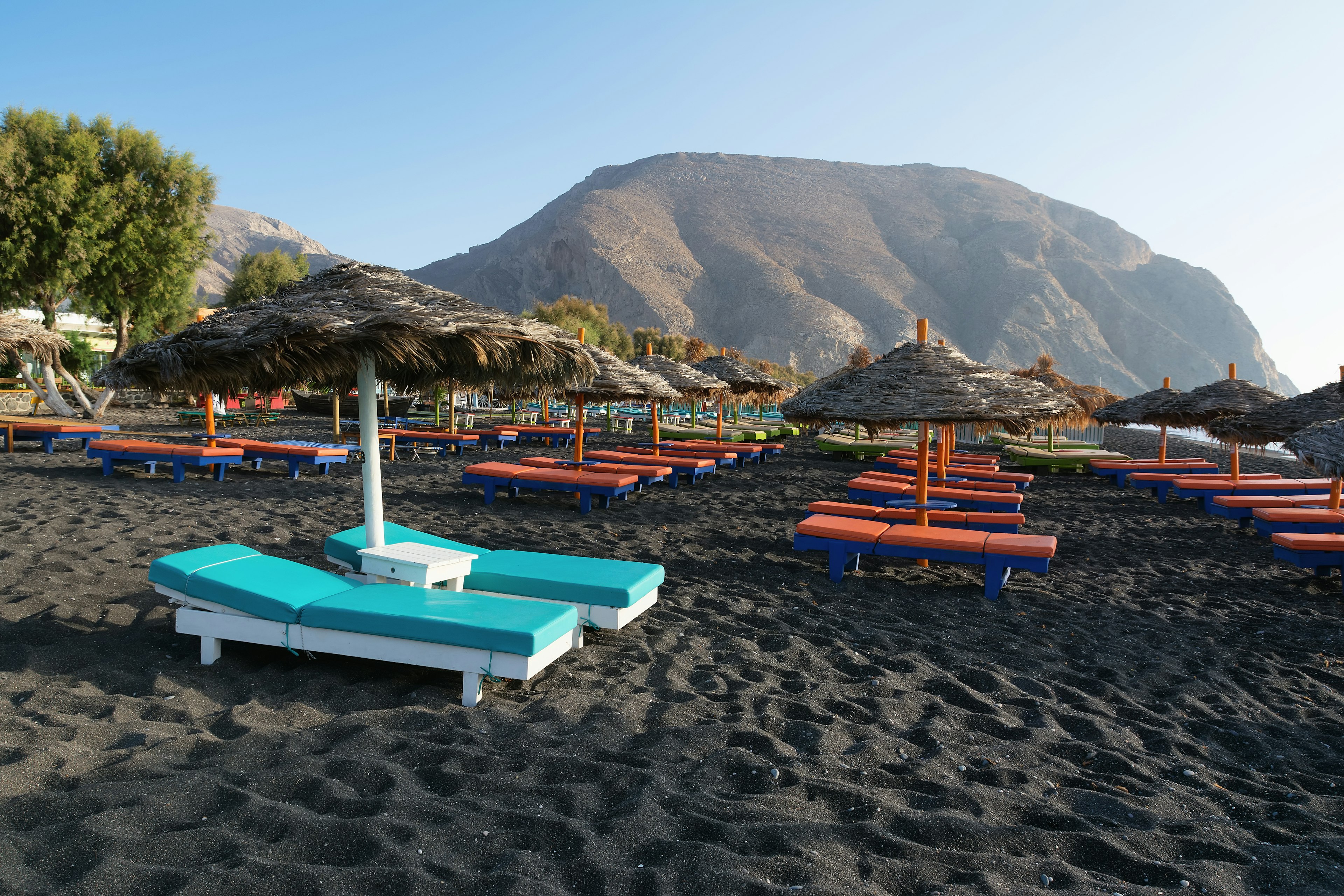 Tanning beds and umbrellas sit empty on a sunny day on a black-sand beach