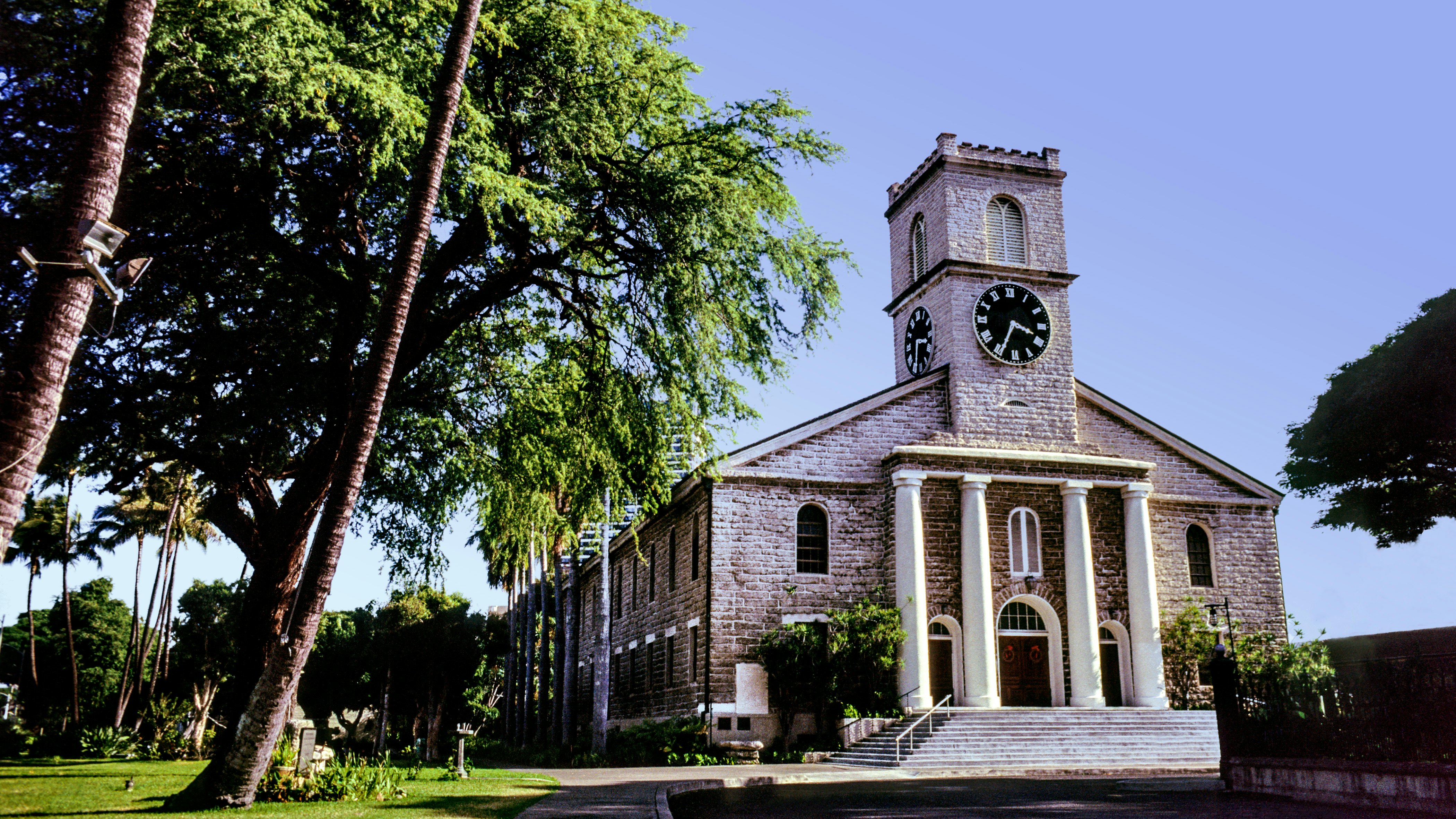 A stone church with a large clock face and Georgian-style columns around its entrance