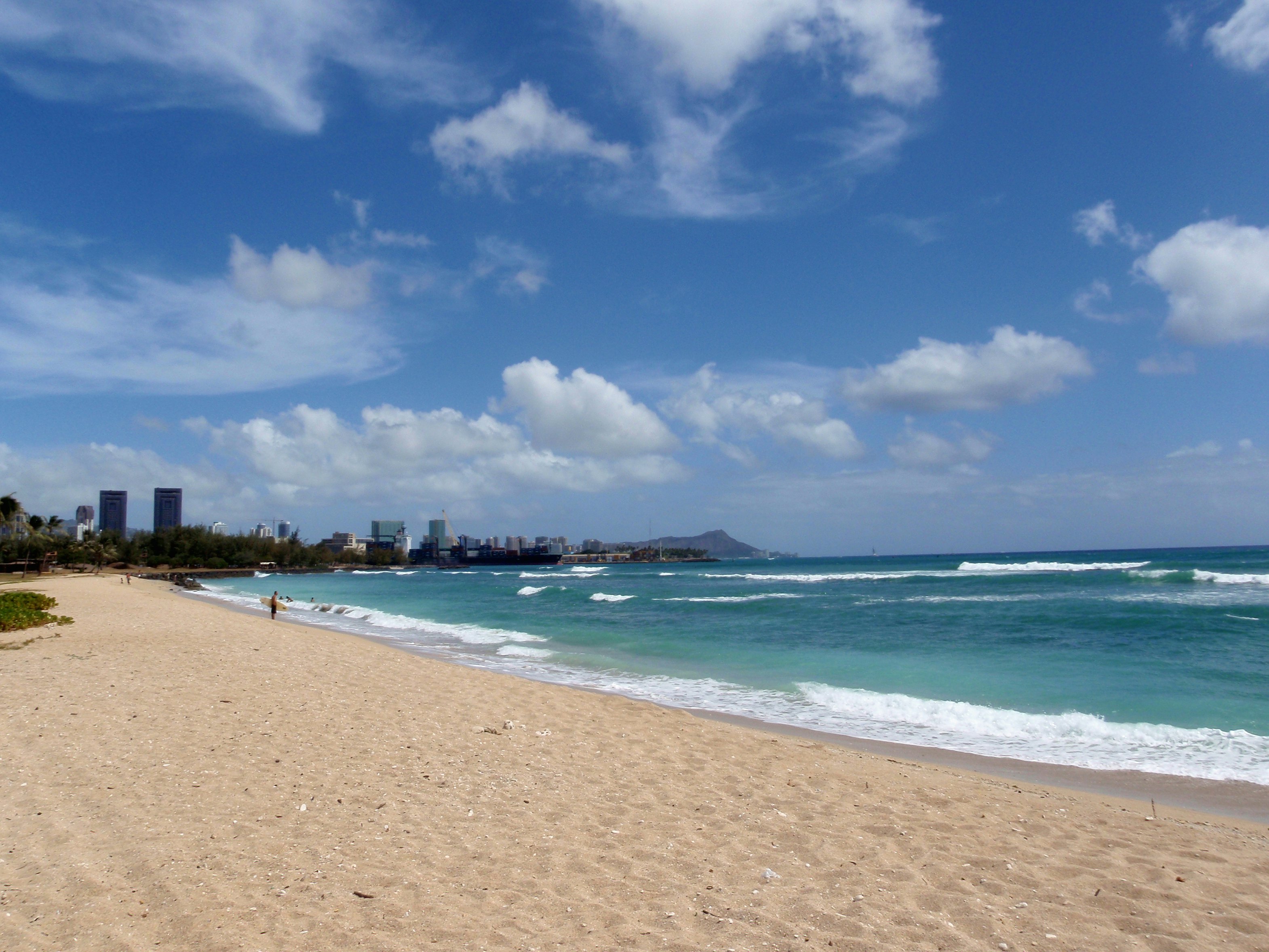 A curved sandy beach with skyscrapers of a city in the distance