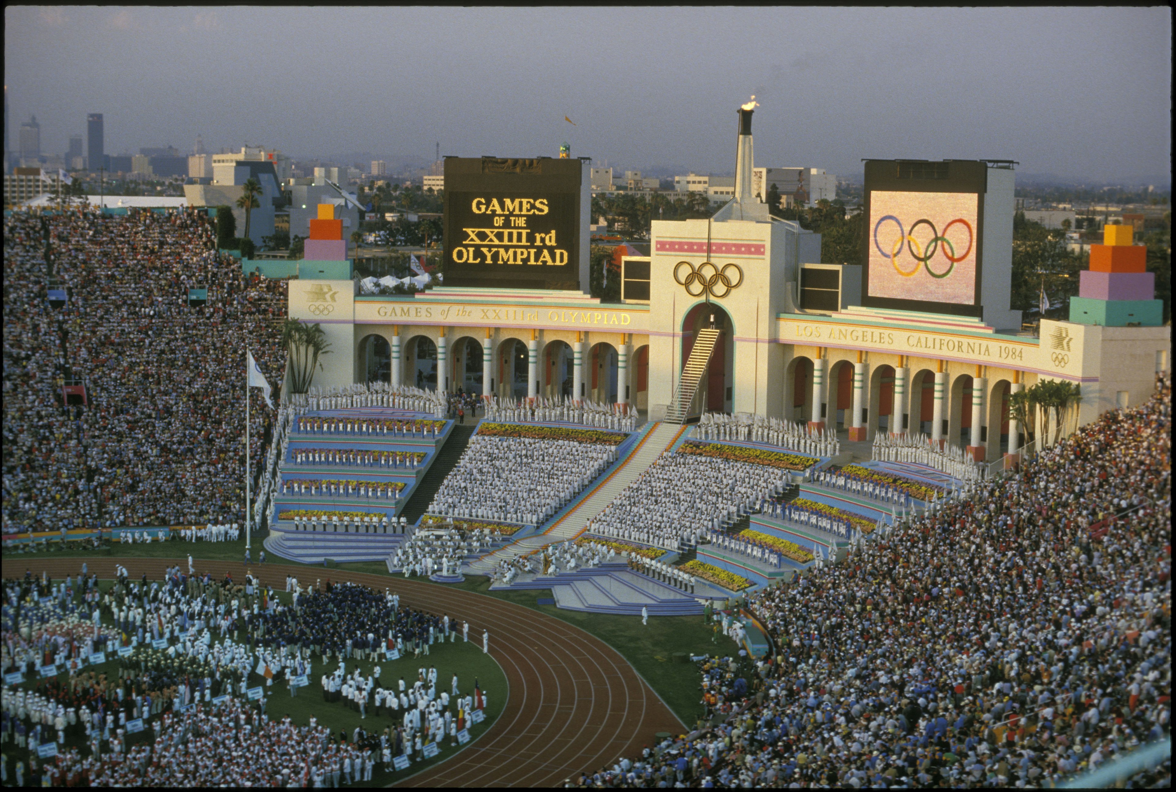 Rafer Johnson lights the Olympic flame at the opening ceremony during the Olympic games in Los Angeles, CA. He is shown at the top of the steps, dressed in white, just below the Olympic rings.