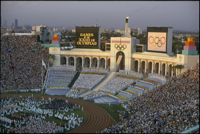 Rafer Johnson lights the Olympic flame at the opening ceremony during the Olympic games in Los Angeles, CA. He is shown at the top of the steps, dressed in white, just below the Olympic rings.
