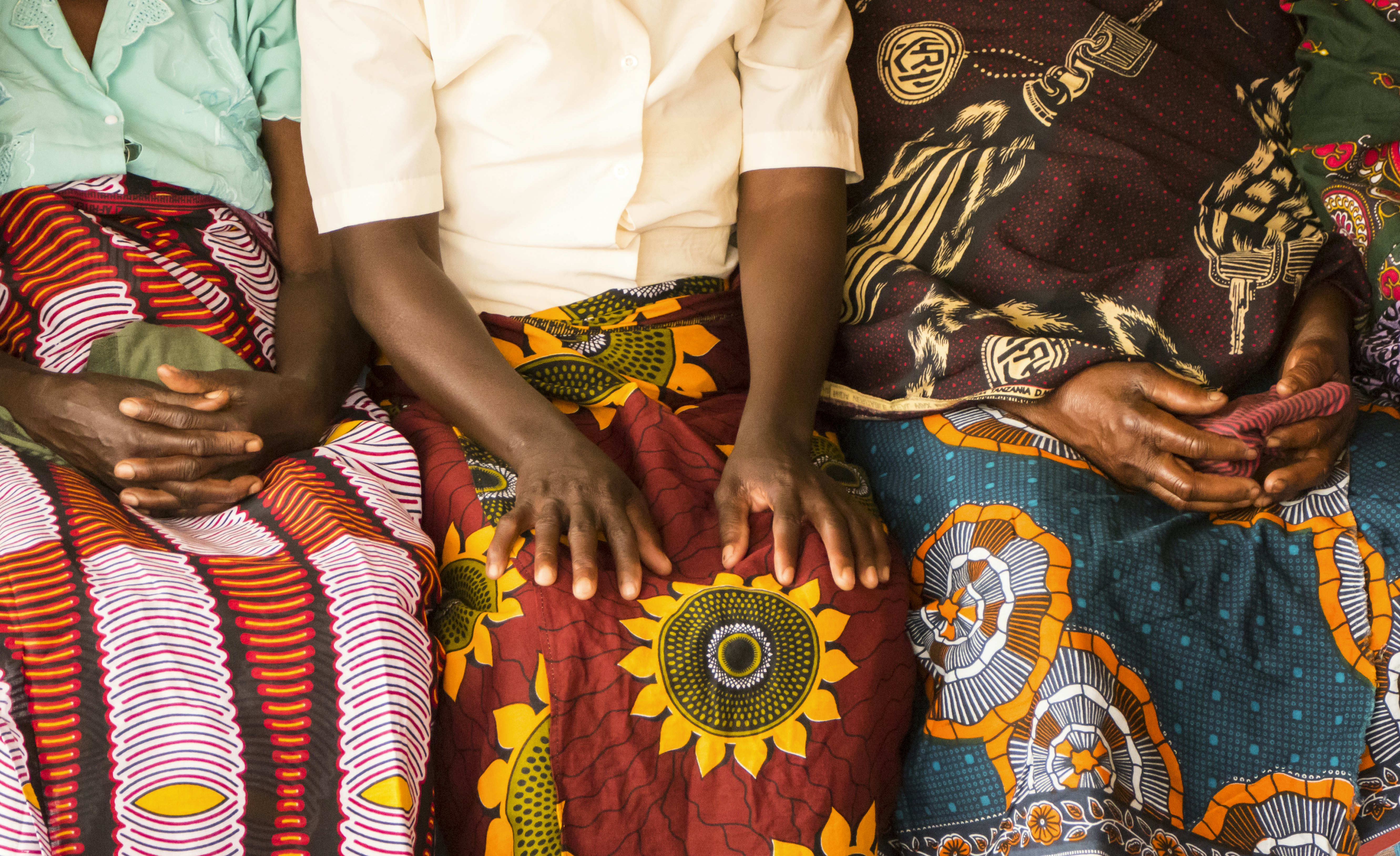 African women sit together wearing traditional clothes with bold colorful patterns