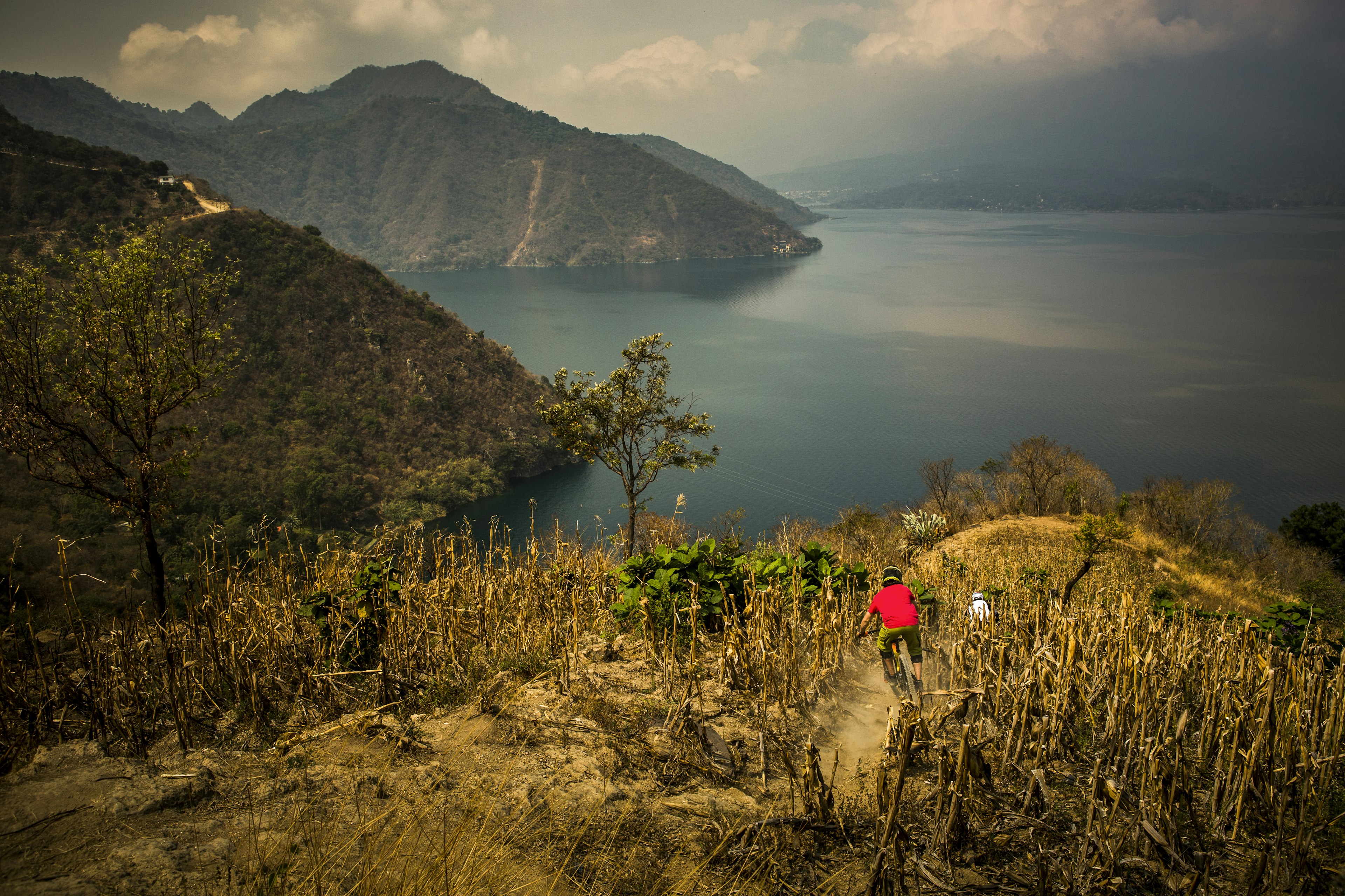 Two mountain bikers on a steep single track on a steep slope leading toward a lake in Guatemala