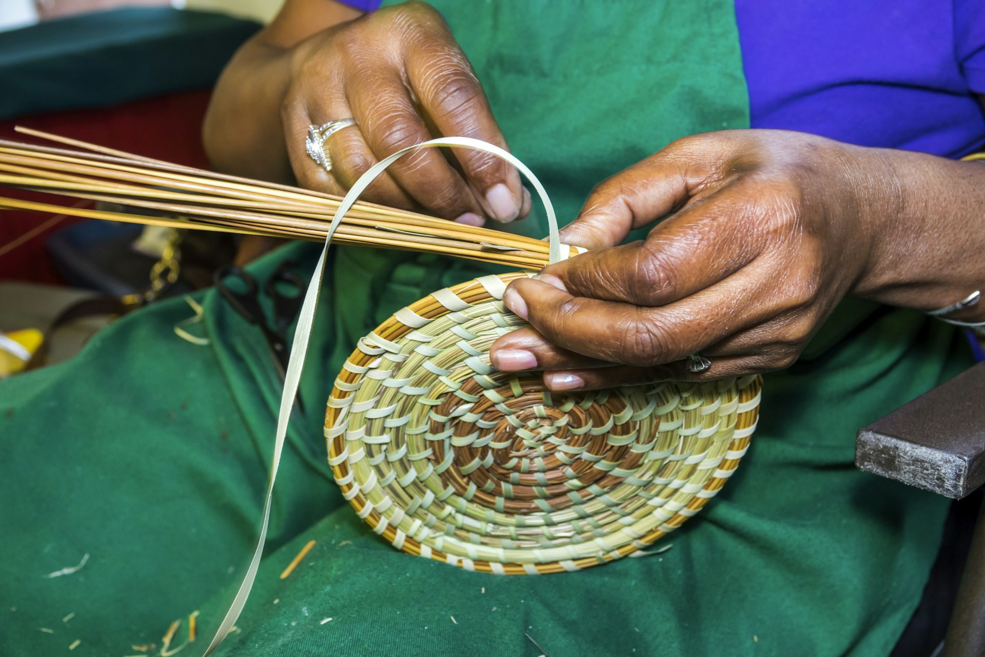 A close-up shot of a woman weaving traditional Gullah baskets from sweetgrass