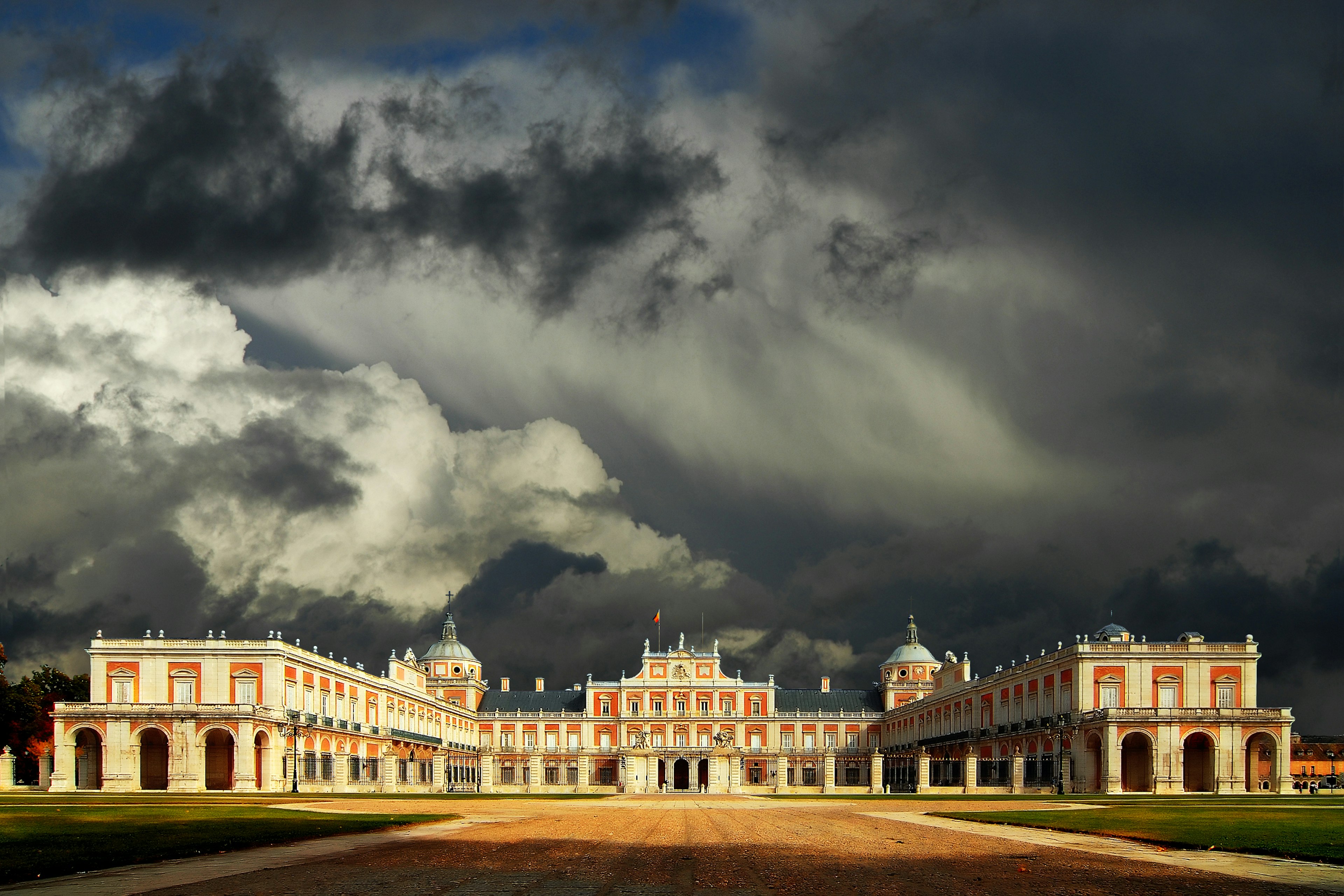 A red-and-white brick palace building under a grey cloudy sky that threatens storms