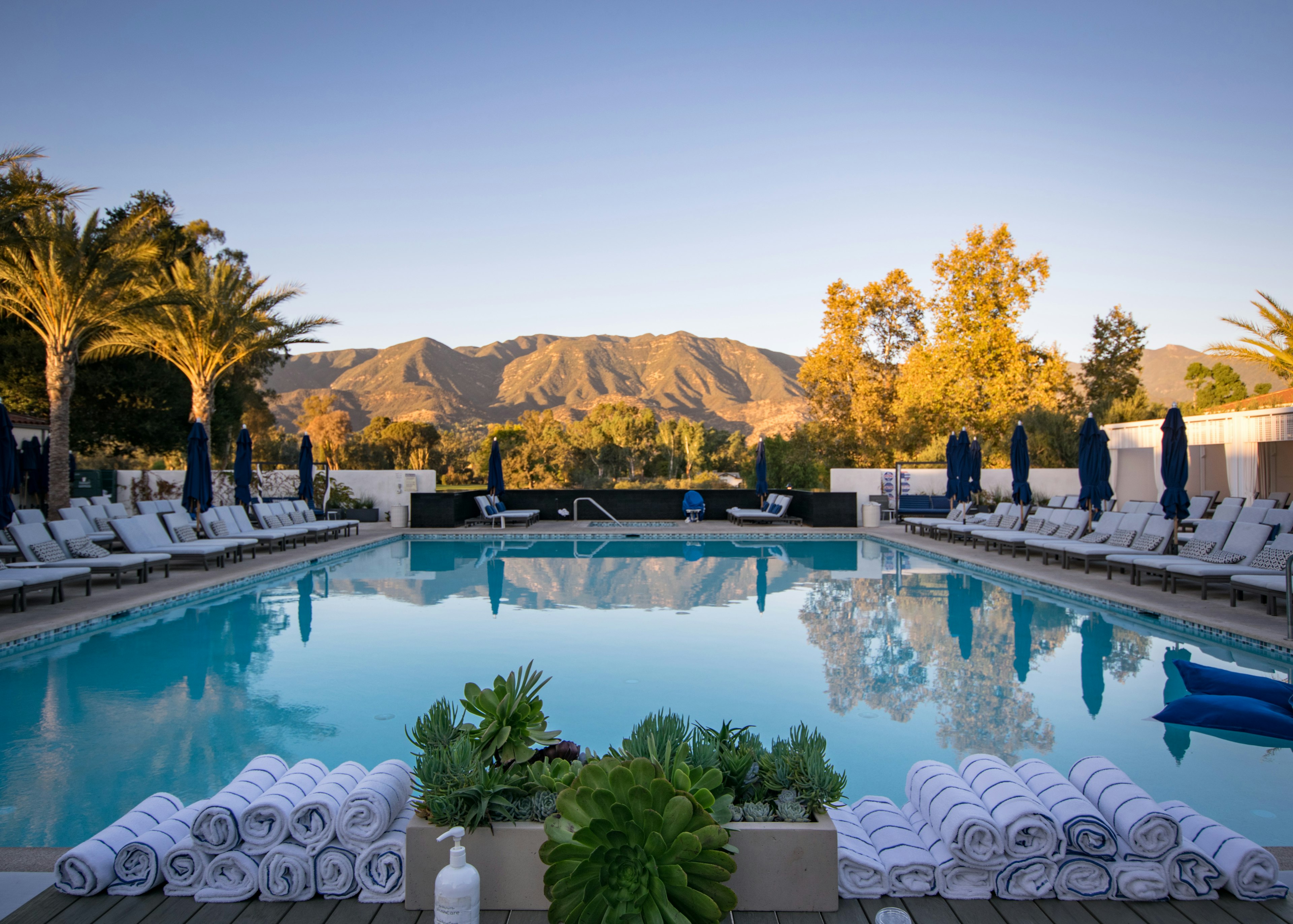 The pool area at Ojai Valley Inn & Spa in autumn, with empty sun loungers and a mountain range in the distance