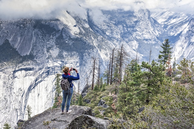 A woman wearing a backpack taking photo in Yosemite