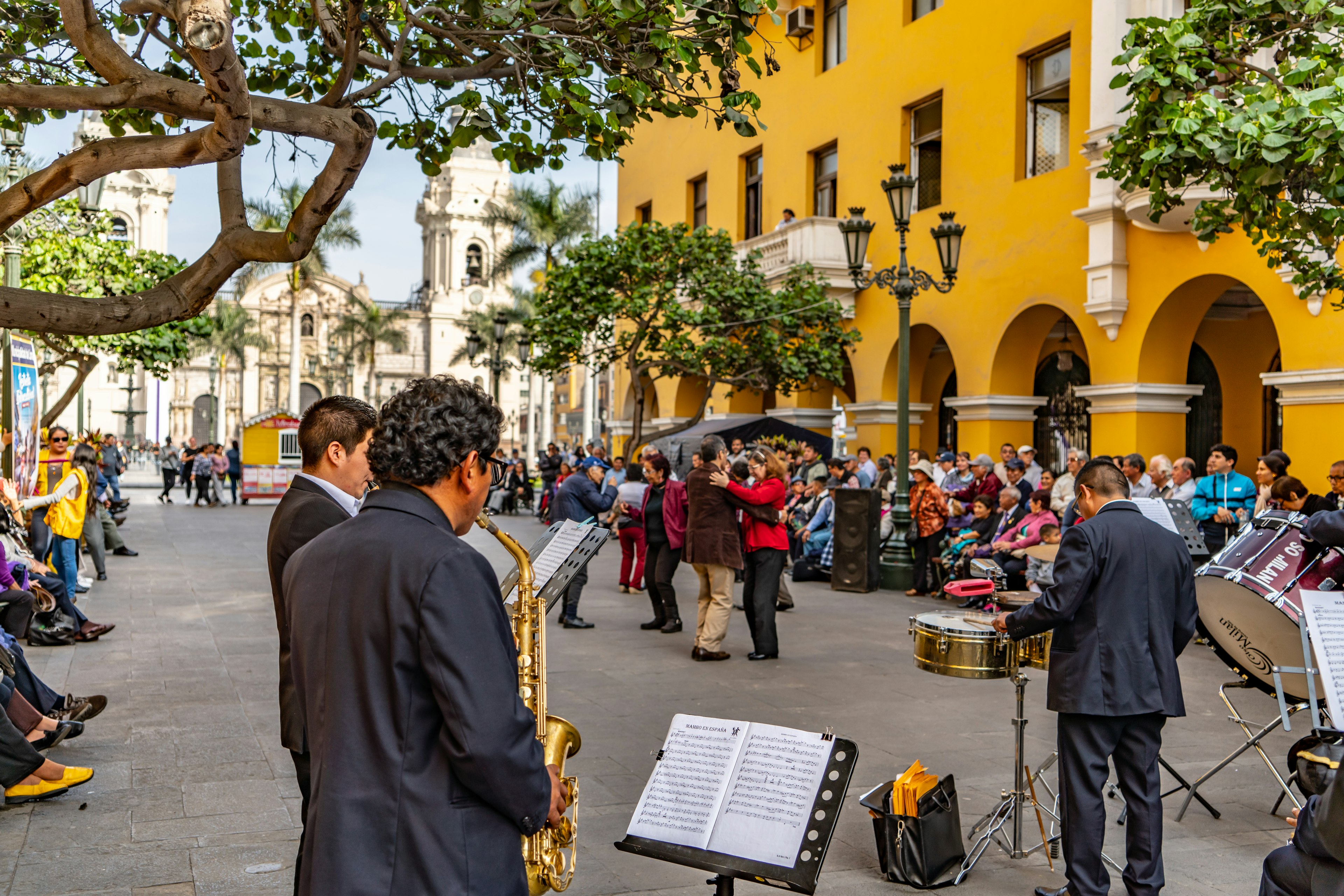 A band performing for a crowd with the bright-yellow buildings of Lima's Plaza de Armas as a backdrop