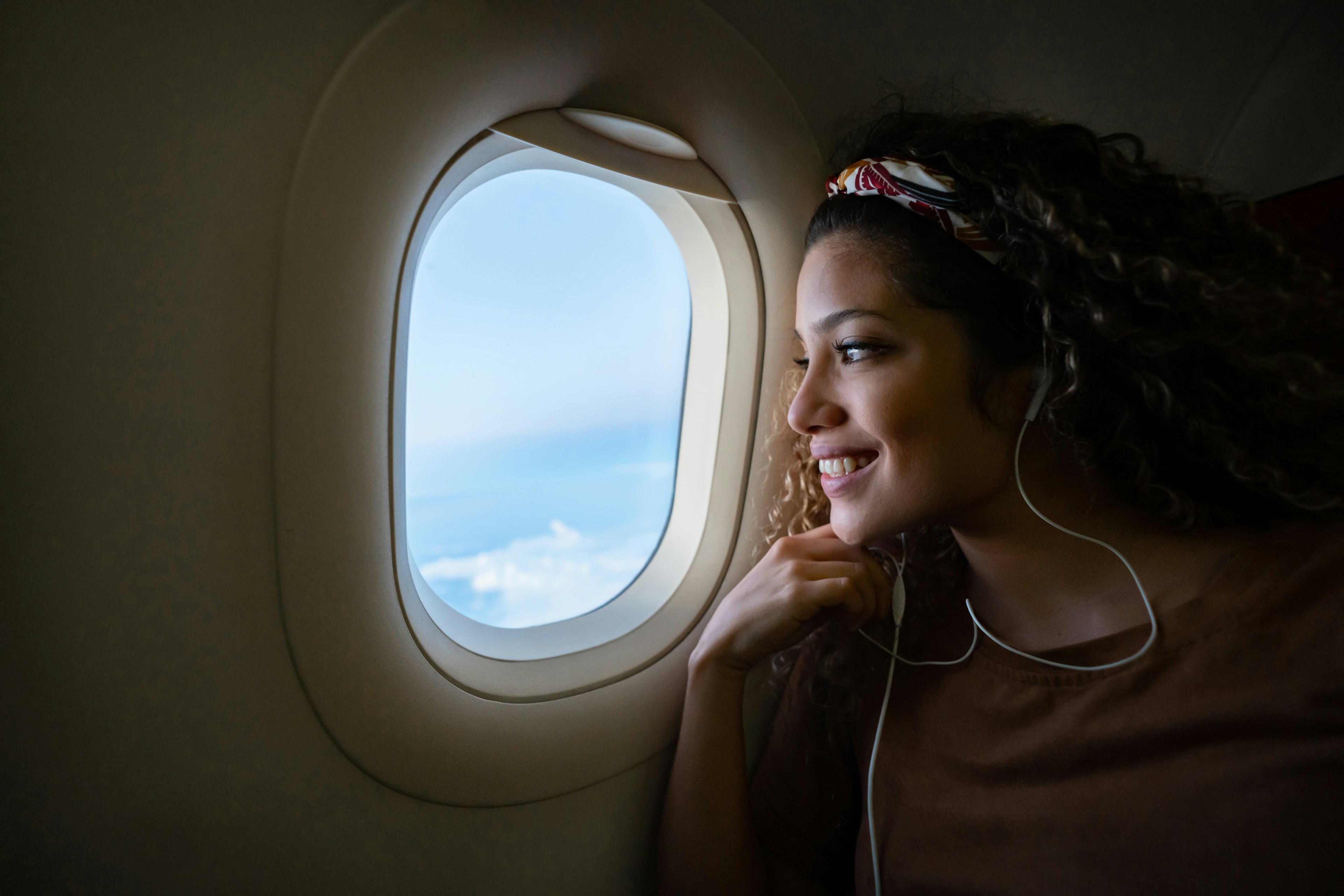 Smiling woman looking out a plane window and listening to music with headphones