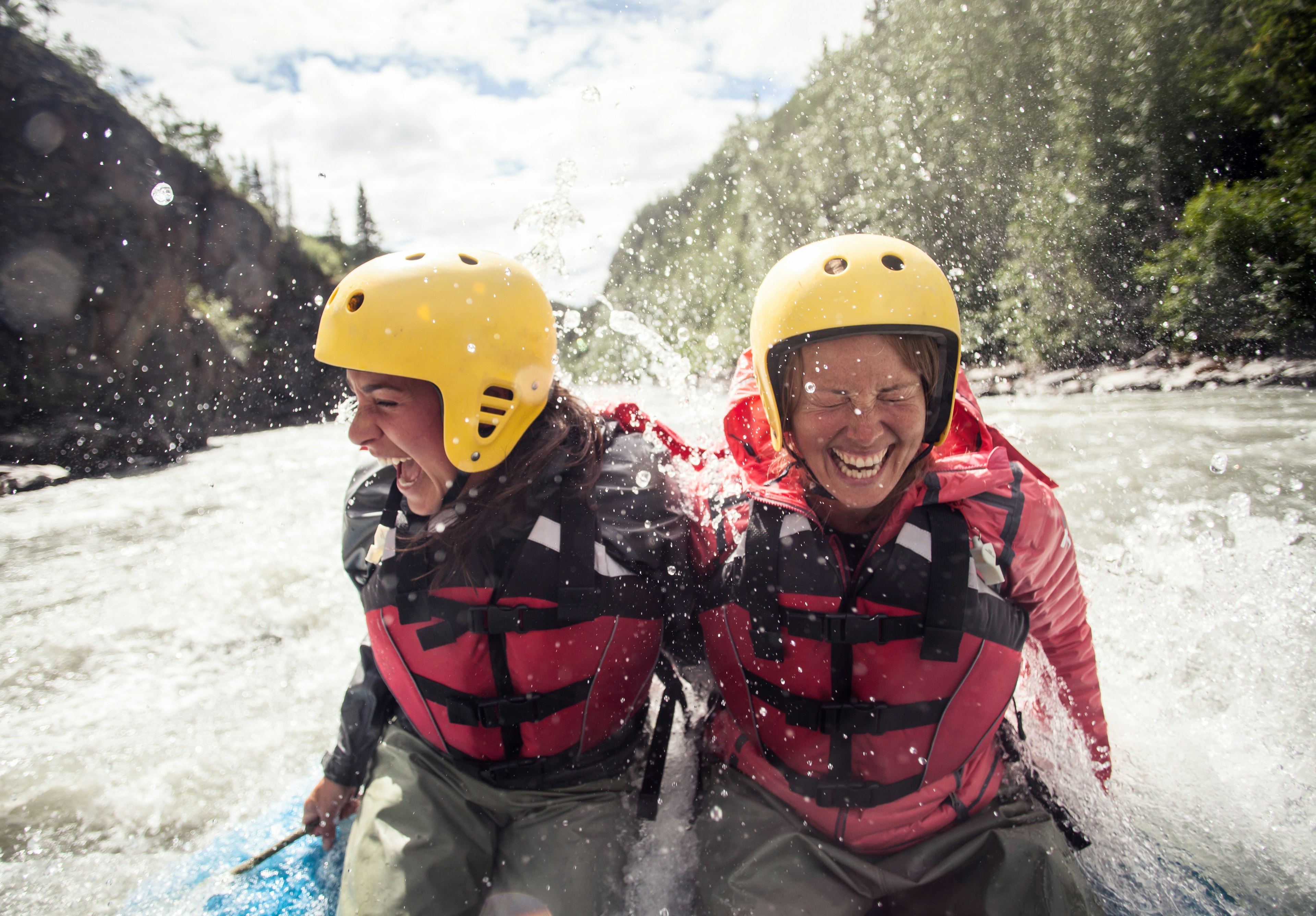 Two friends in yellow helmets laugh and scream as their raft travels through rapids