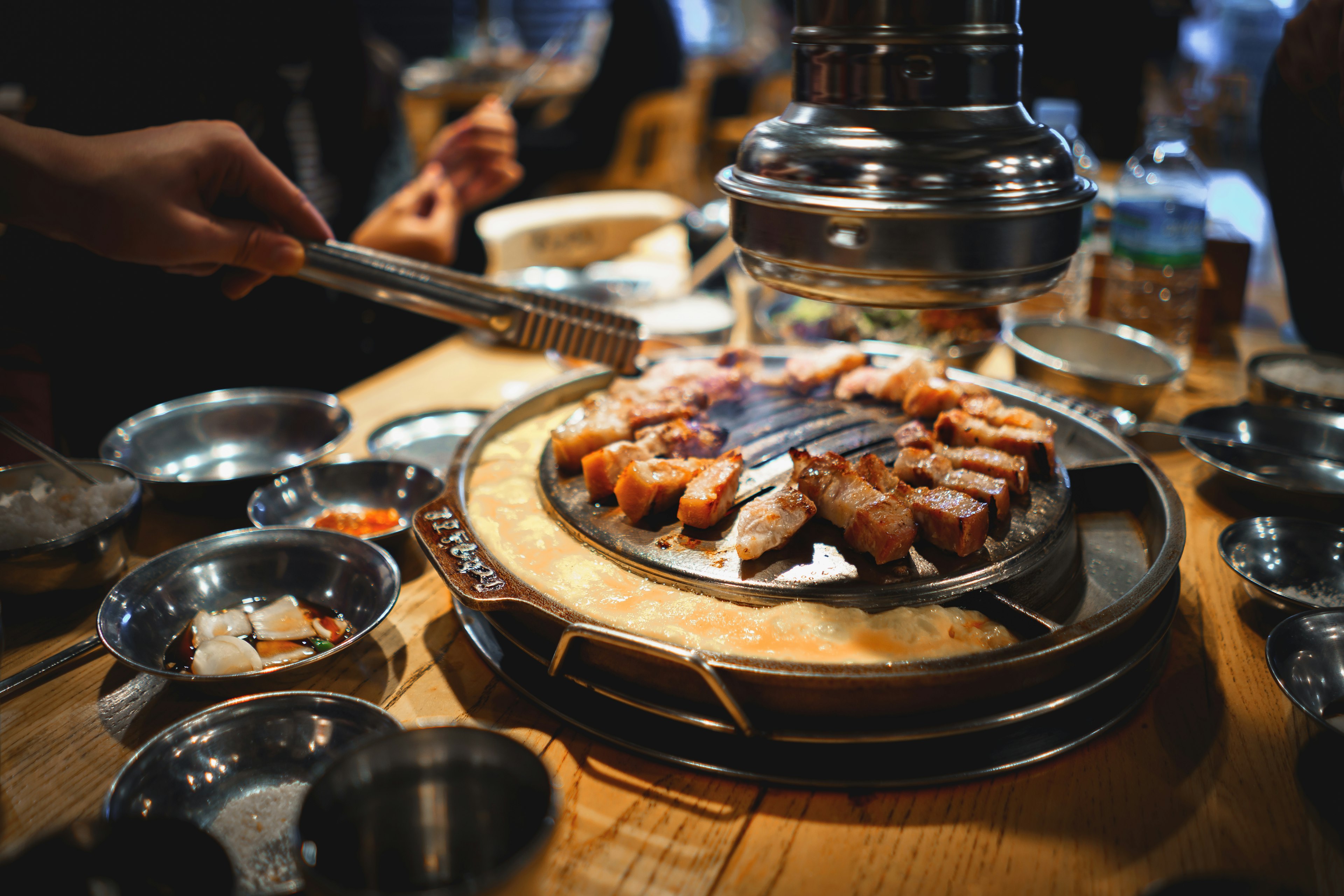 A diner with chopsticks reaches for meat on the grill at a barbecue restaurant, Seoul, South Korea