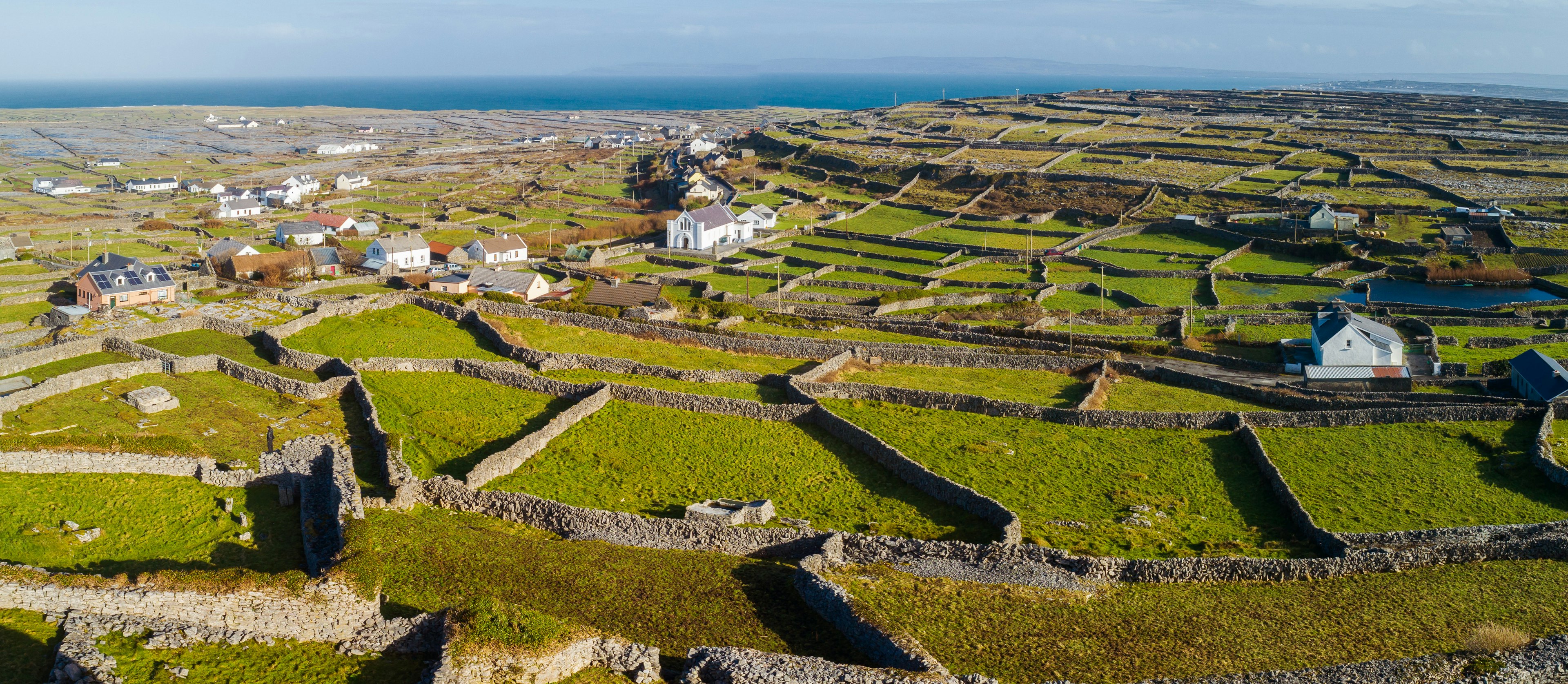 Aerial shot of an island with stone walls dividing up plots of land, and a few scattered white cottages among the vast green landscape