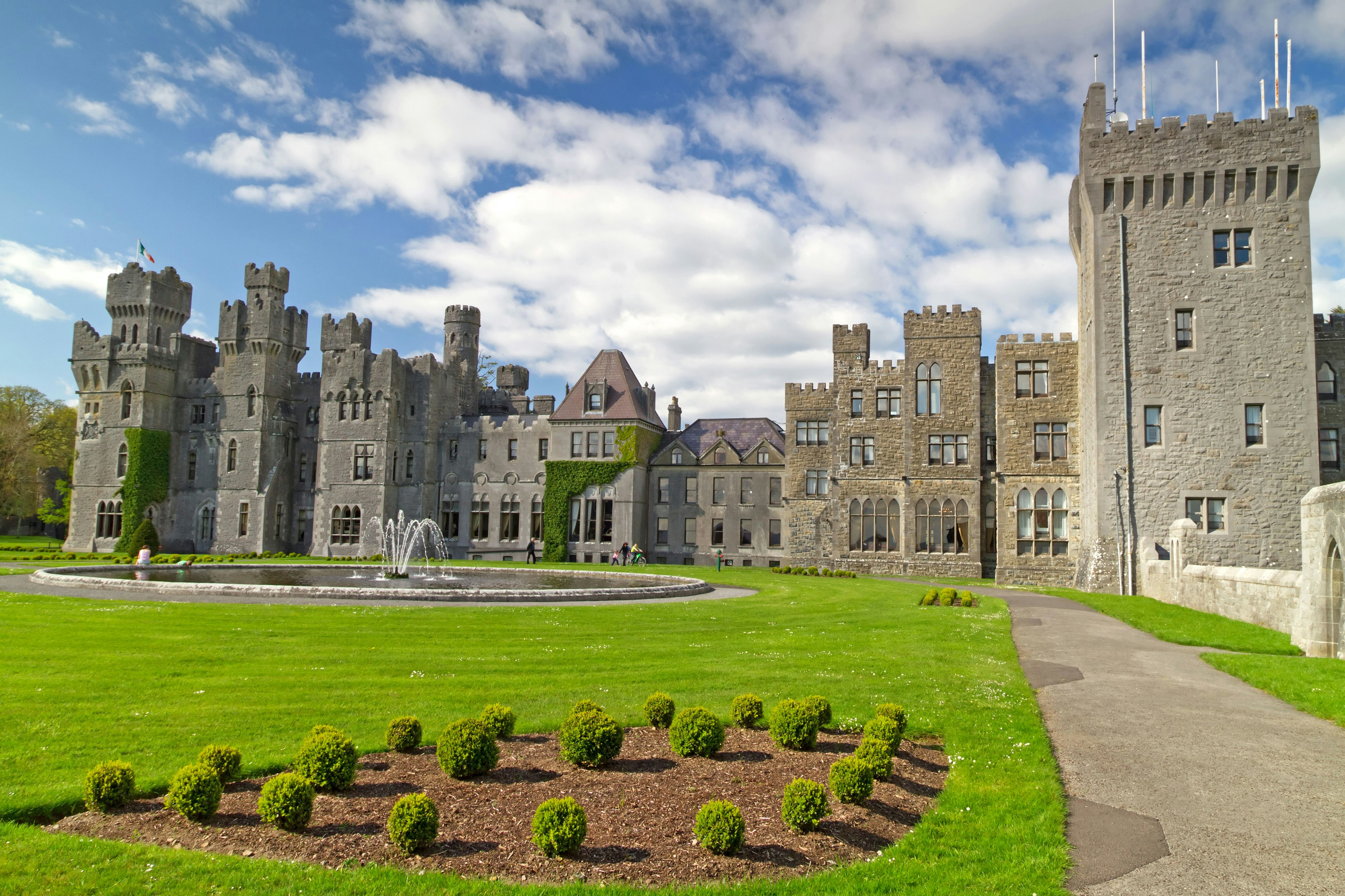 Medieval Ashford castle and gardens under a cloudy sky.