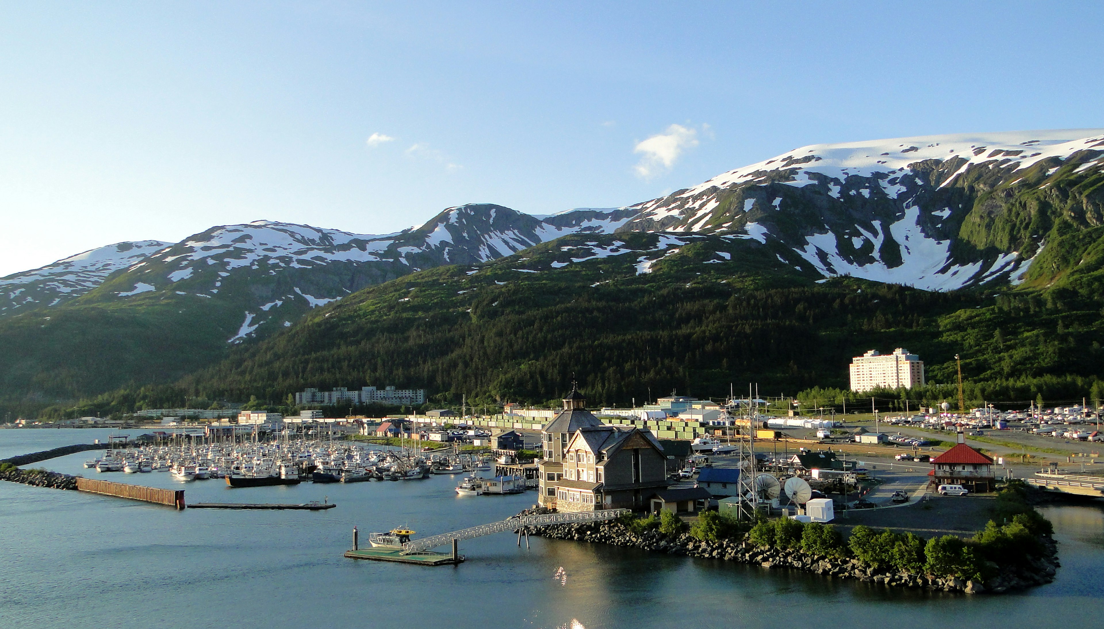 Boats in the harbor of Whittier, Alaska, with snow-fringed mountains rising behind the town