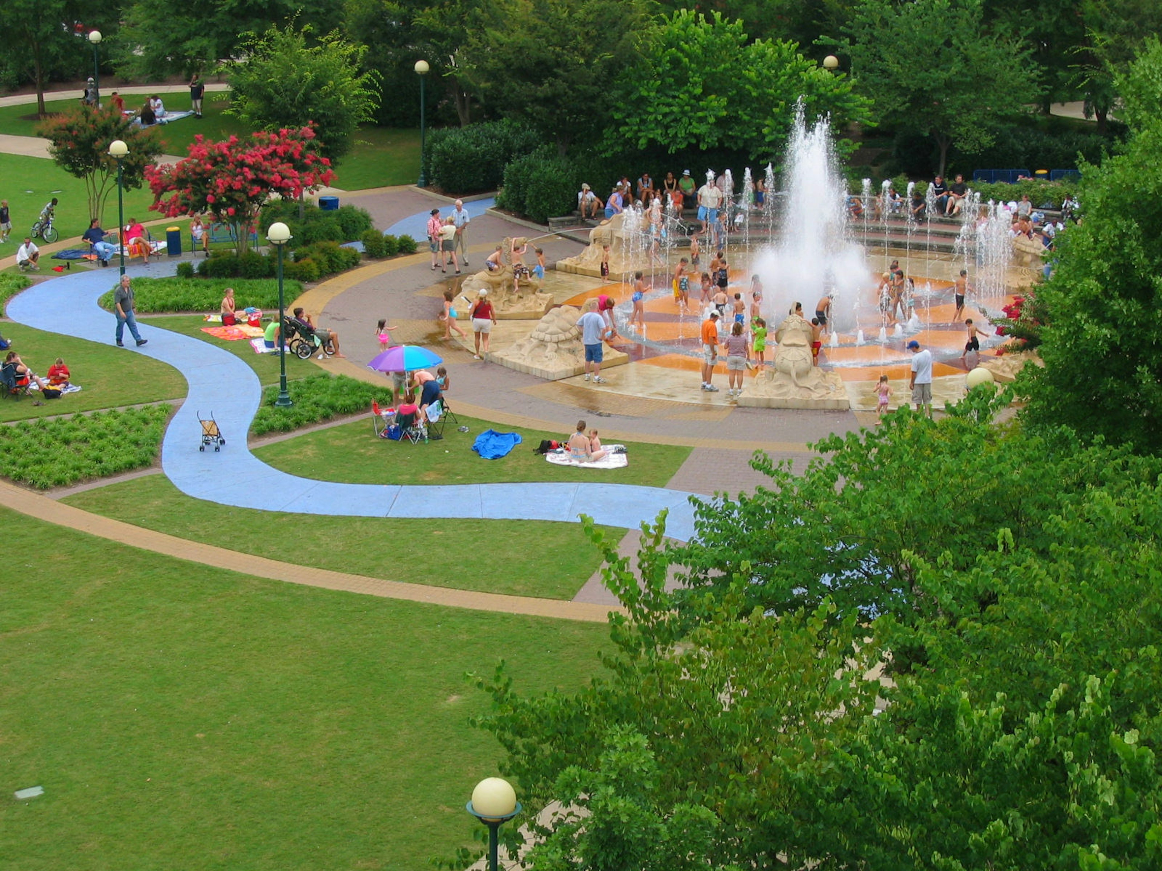 An aerial shot of a park with people playing in a fountain