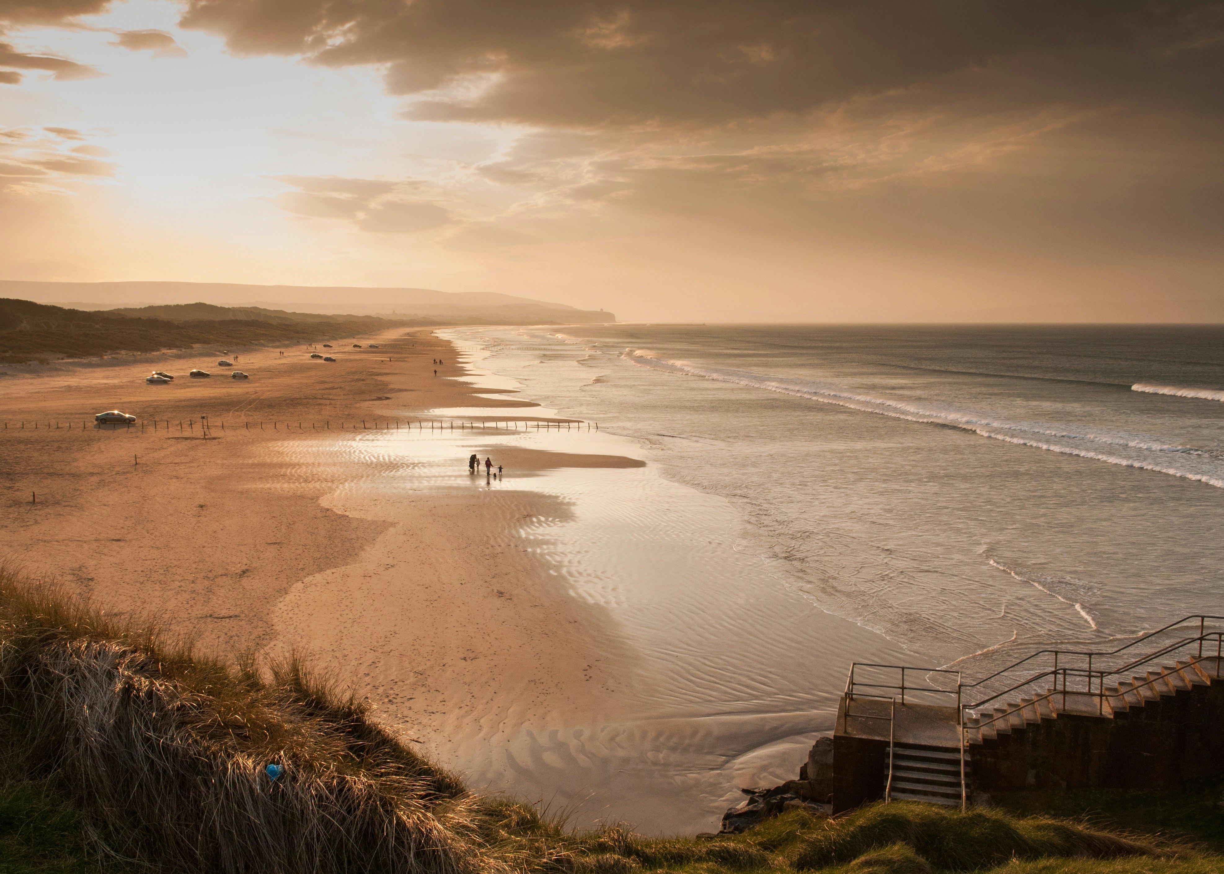 An especially wide beach that stretches into the distance. Some cars are parked on the beach