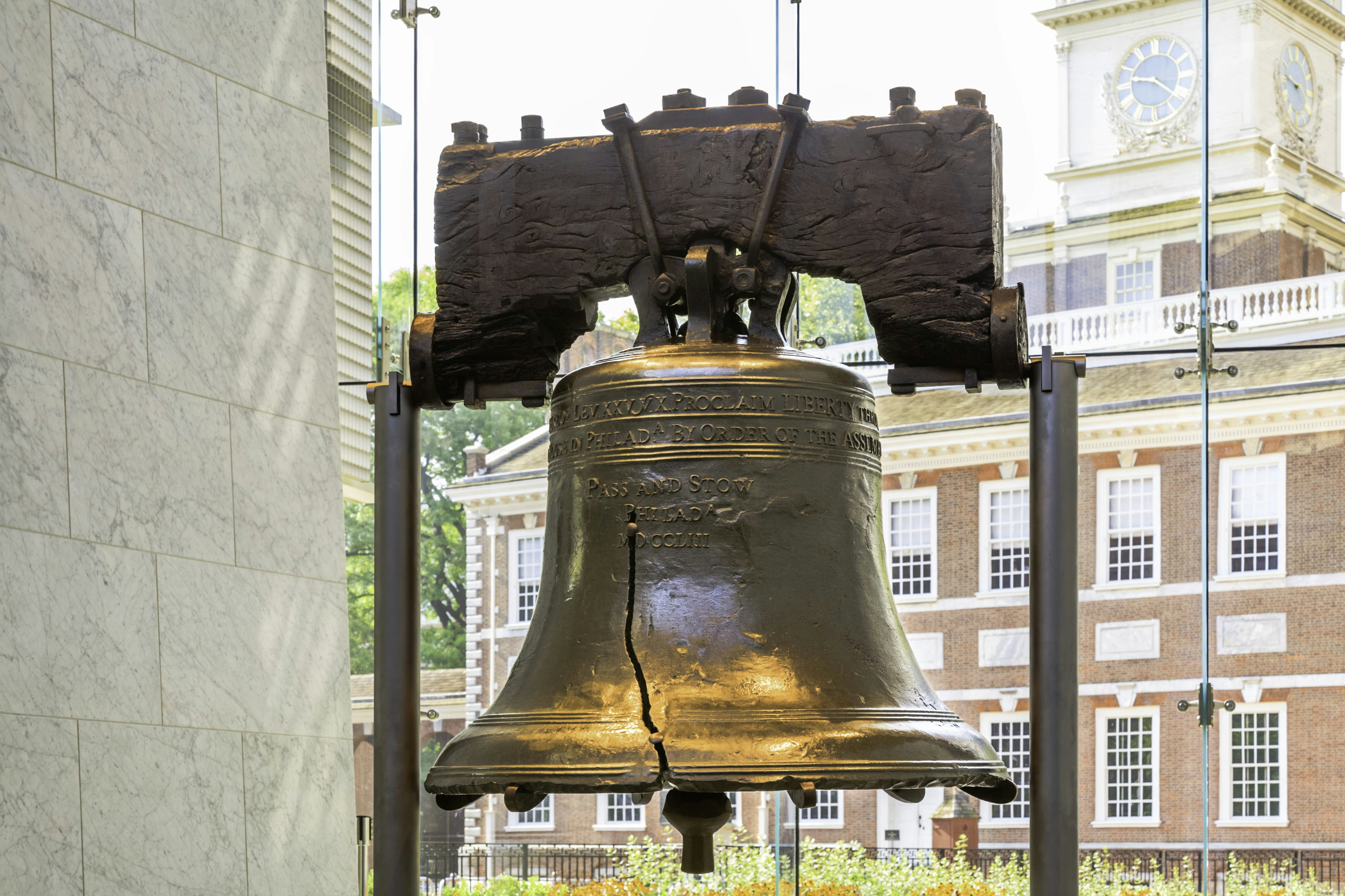 A large bell with a crack running upwards through it, mounted in a glass building