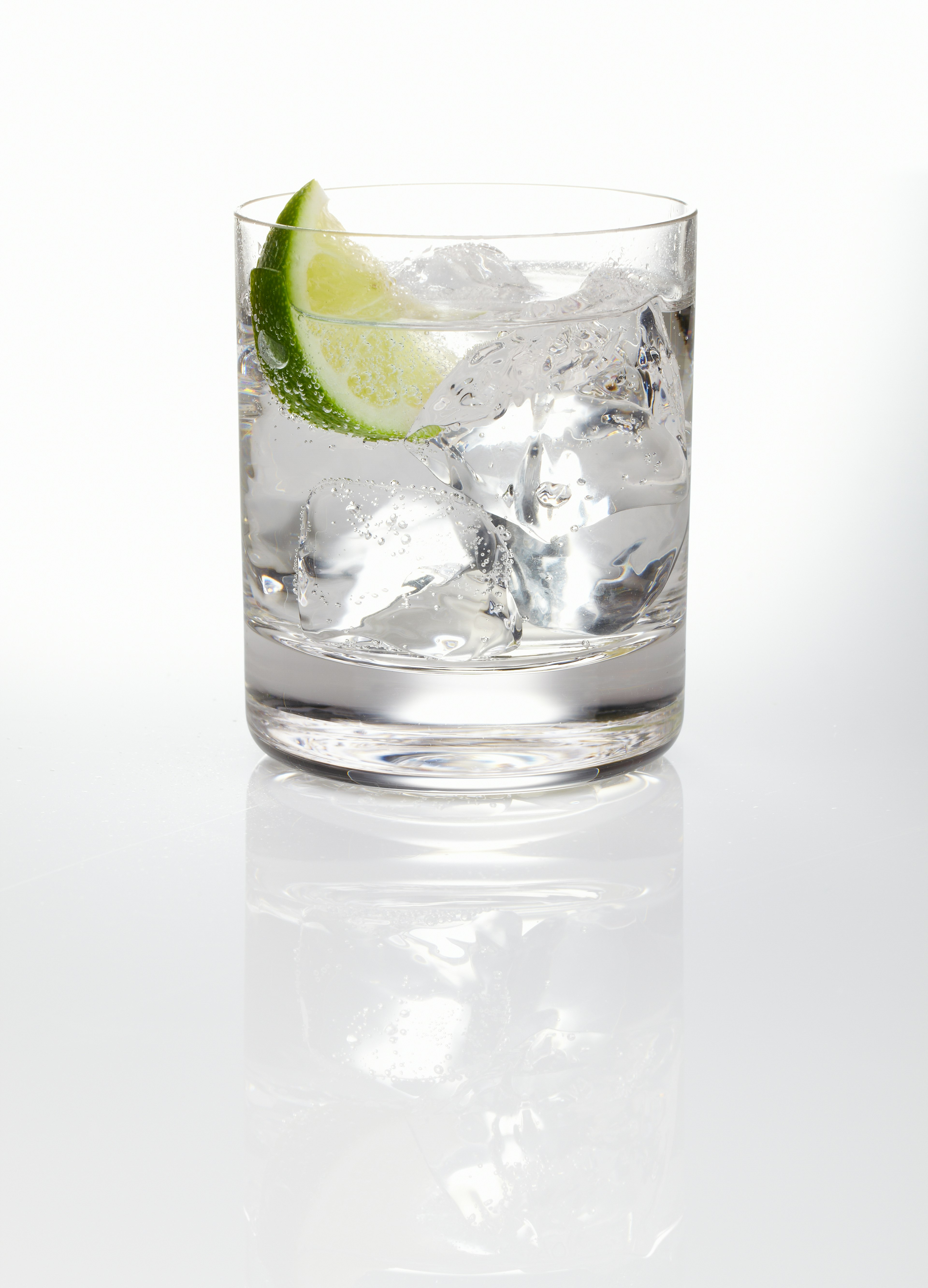 A glass of gin and tonic with ice and a slice of lime