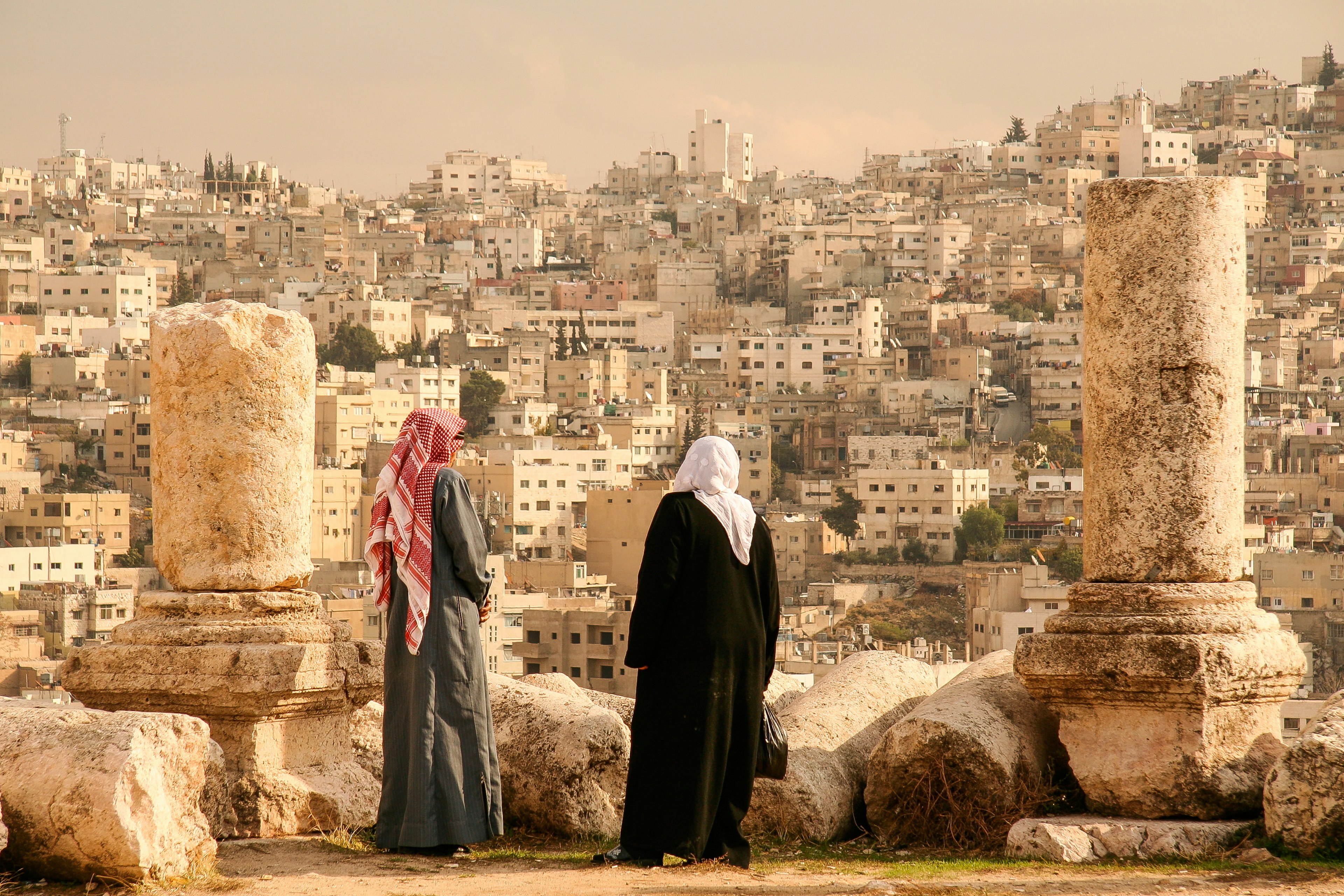 Two people in traditional Jordanian dress look out over the heavily developed hillsides of Amman