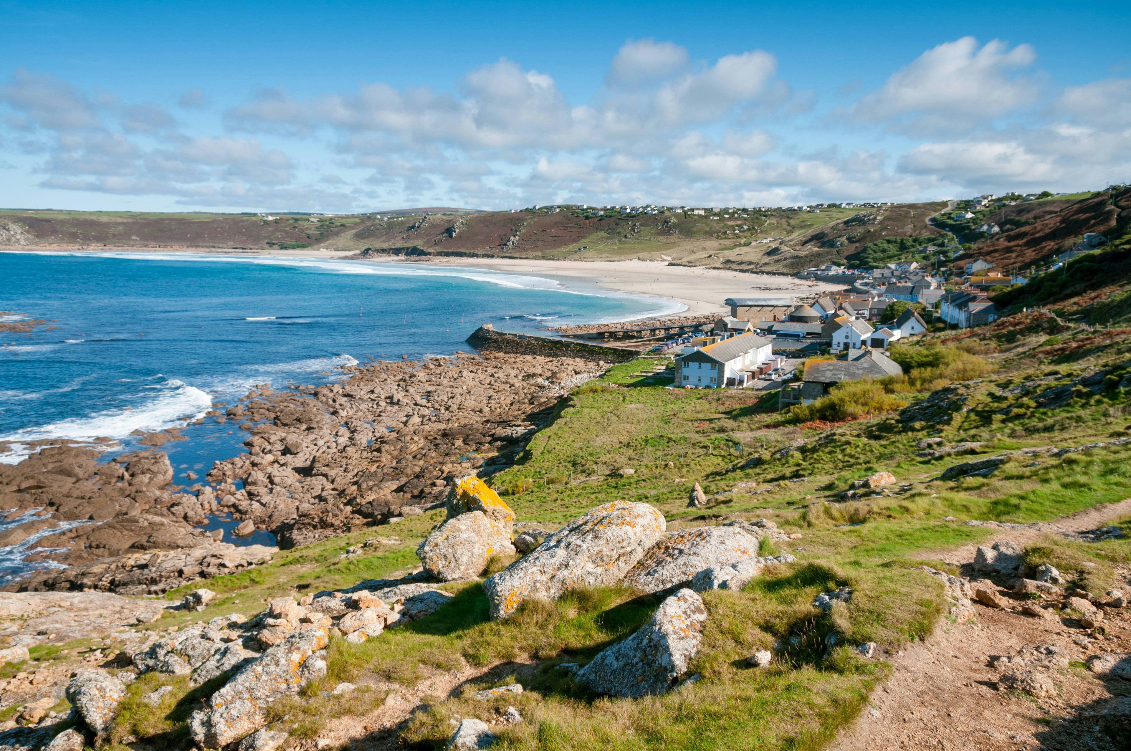 A wide sandy cove with rocky edges. The cliff is lined with white cottages