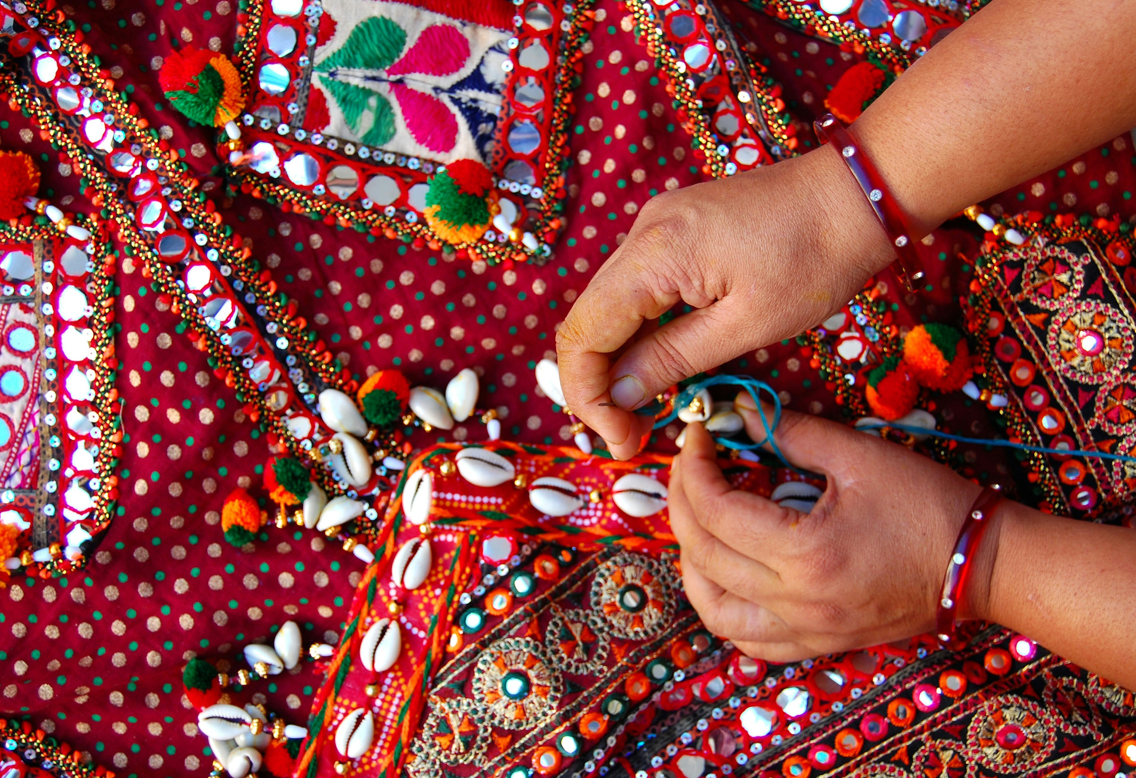 A women embroiders patterns on red fabric – a tradition from the Rann of Kachchh in Gujarat, India.