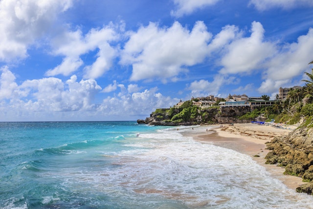 Aerial view of Crane Beach with white foam waves crashing on the sand. You can see a hotel on the high green cliffs.