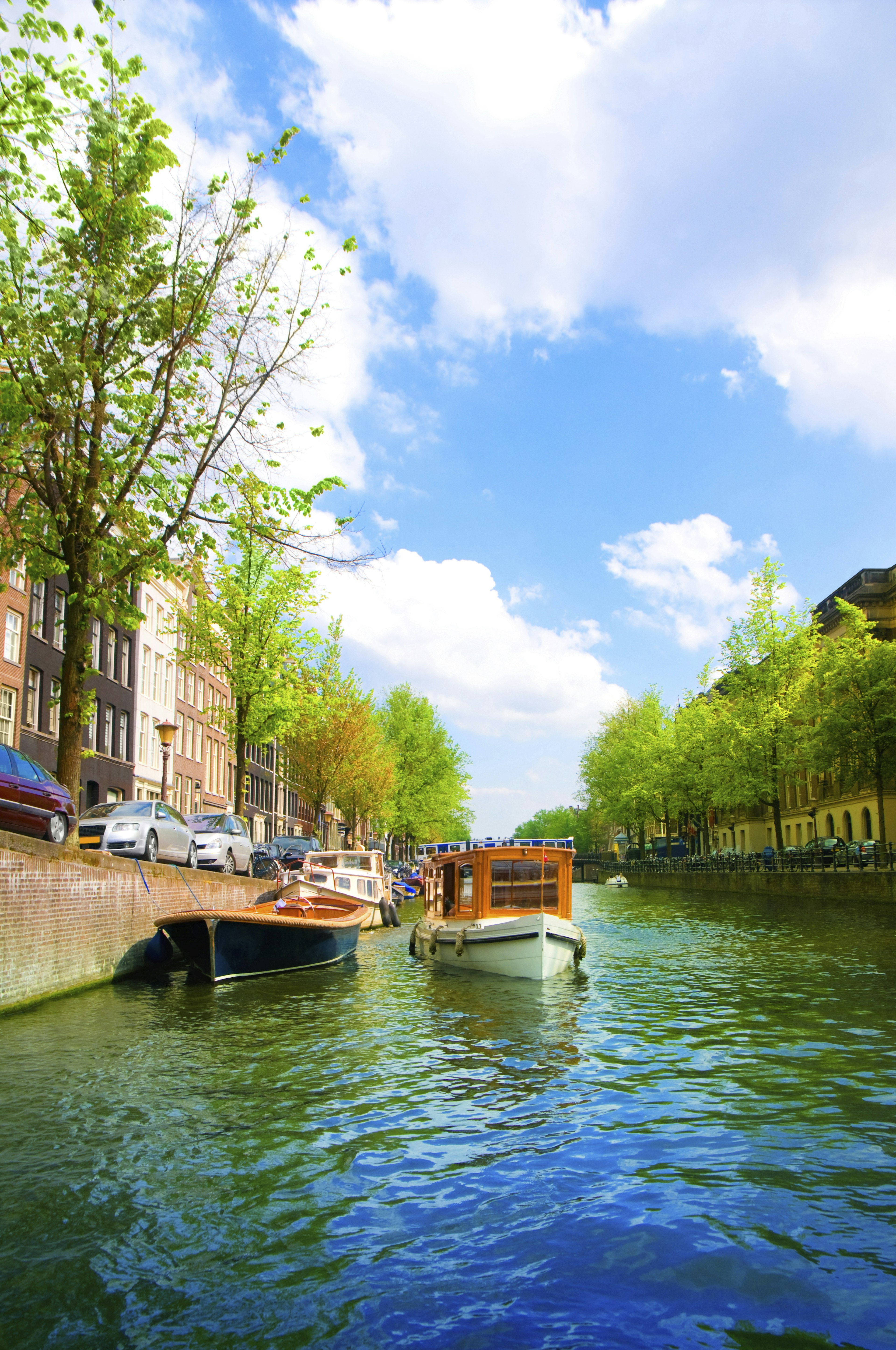 A blue-green canal in Amsterdam, with two small boats moored against a brick wall