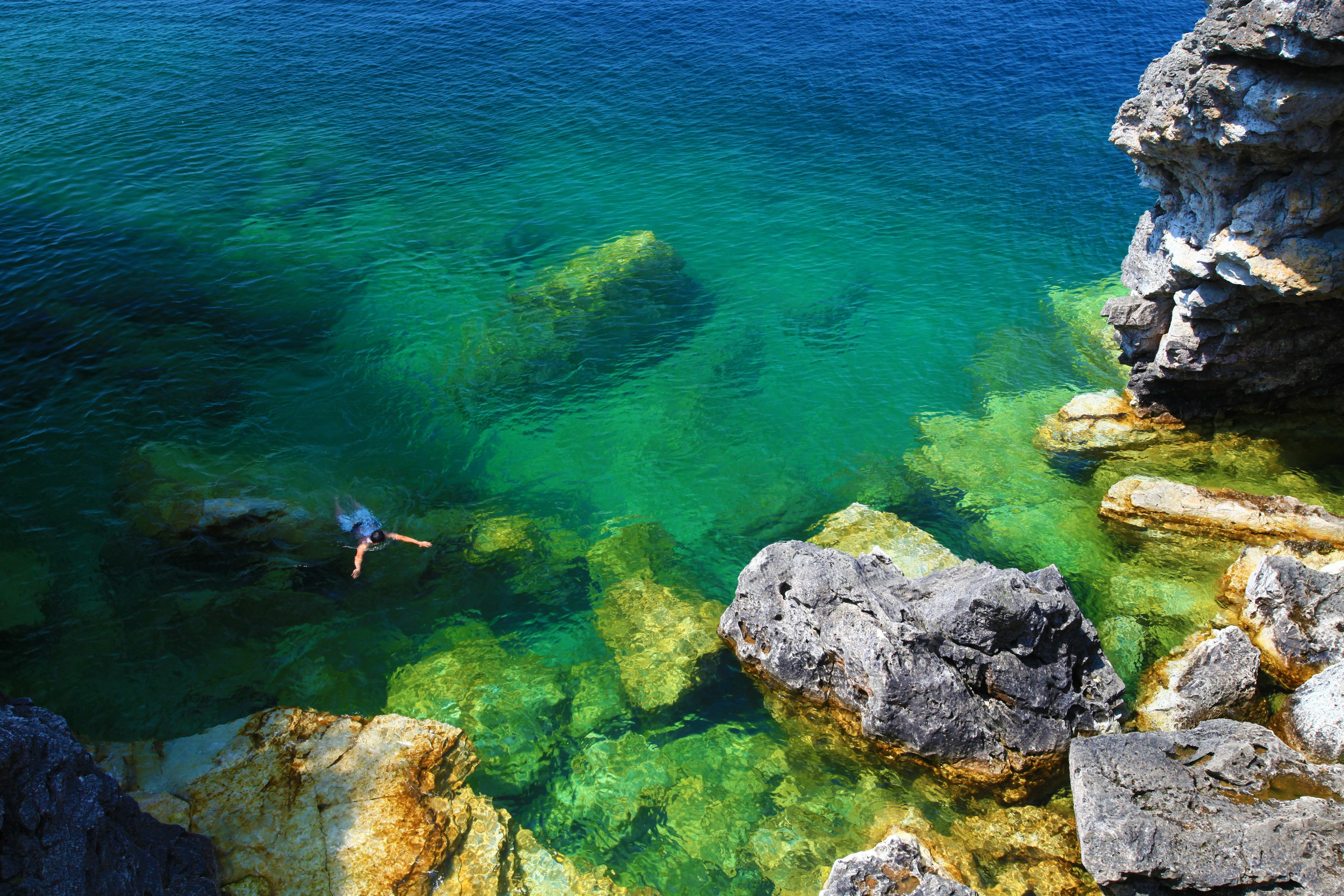 A swimmer in turquoise waters near a rocky shore