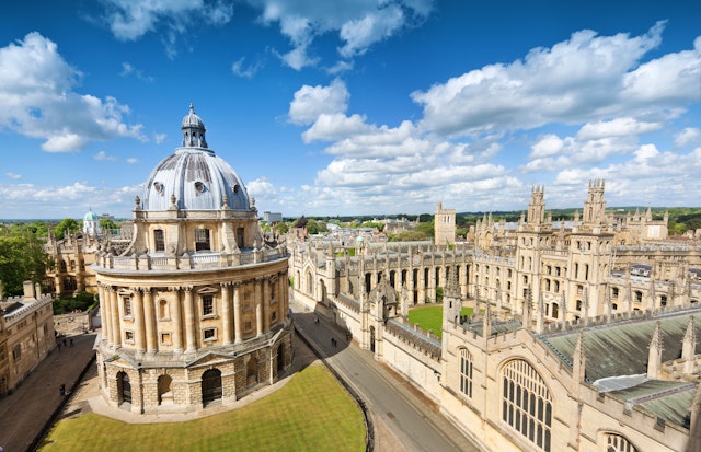 The sandstone-colored buildings of Oxford, including a round building in the middle of a green, and spires on surrounding buildings