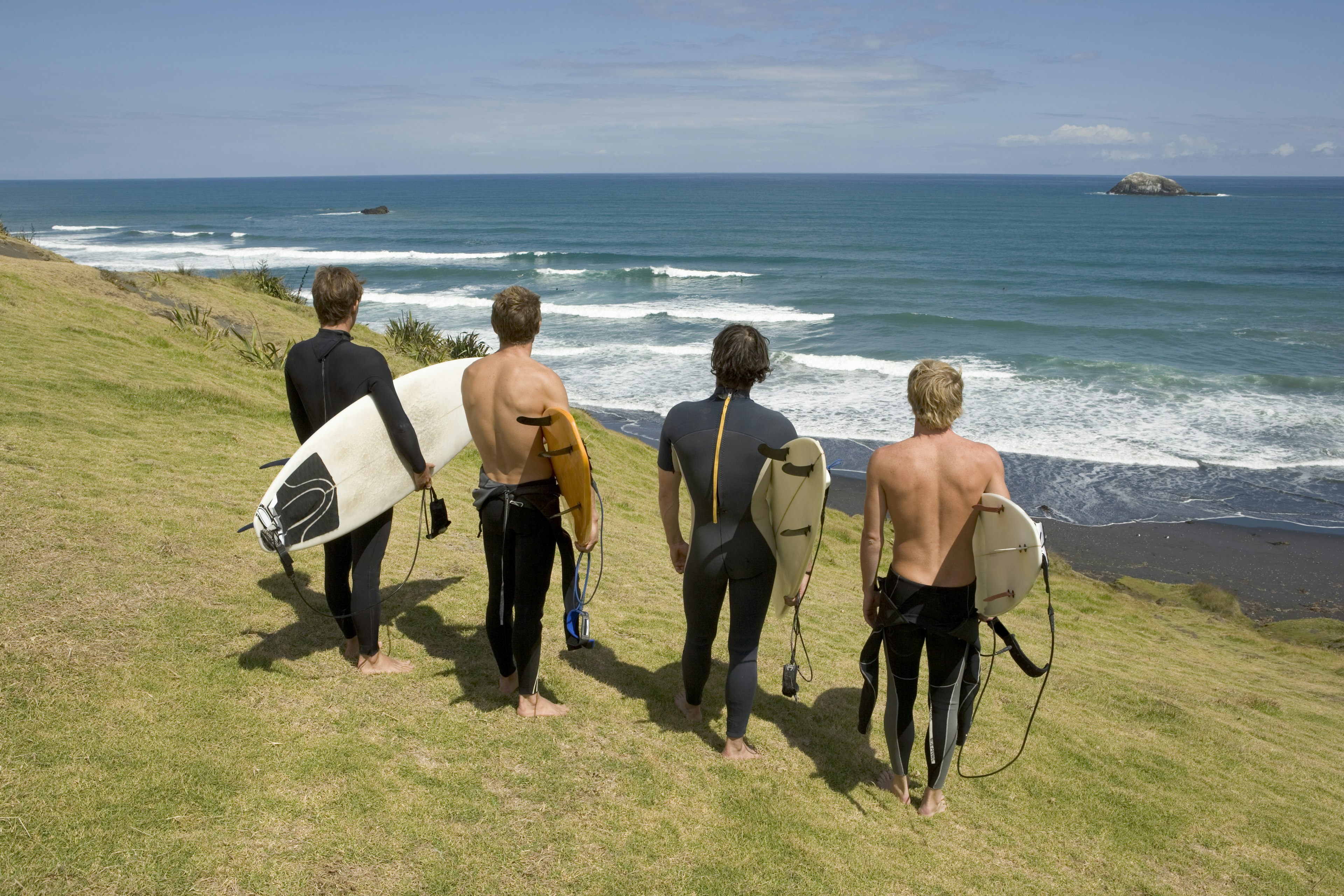 Four surfers standing on cliff top overlooking sea in Auckland New Zealand