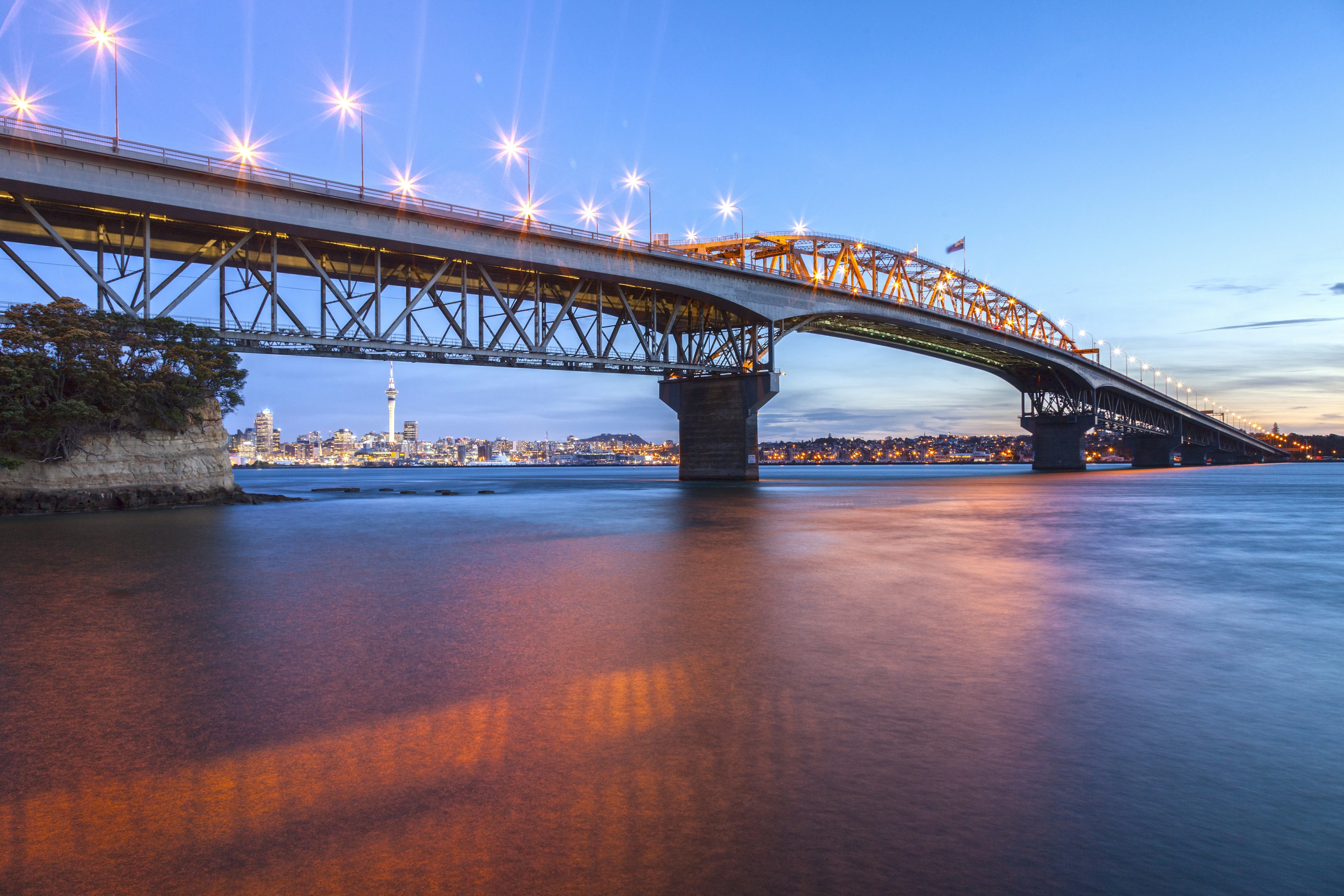 Auckland Harbour Bridge at twilight from Northcote Point, with pink light reflected in the water