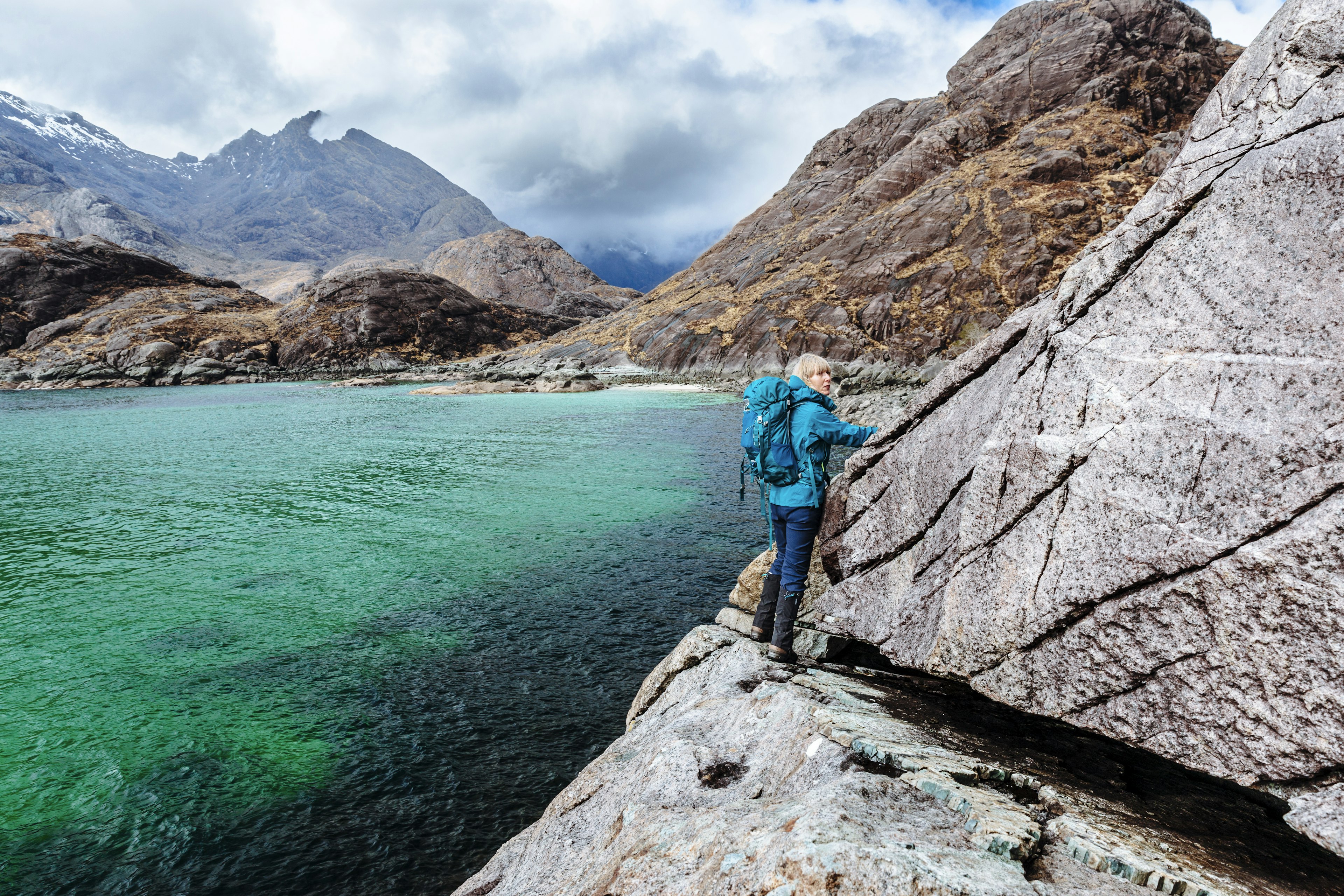 A woman hugging a tight path alongside some rocks above a lake