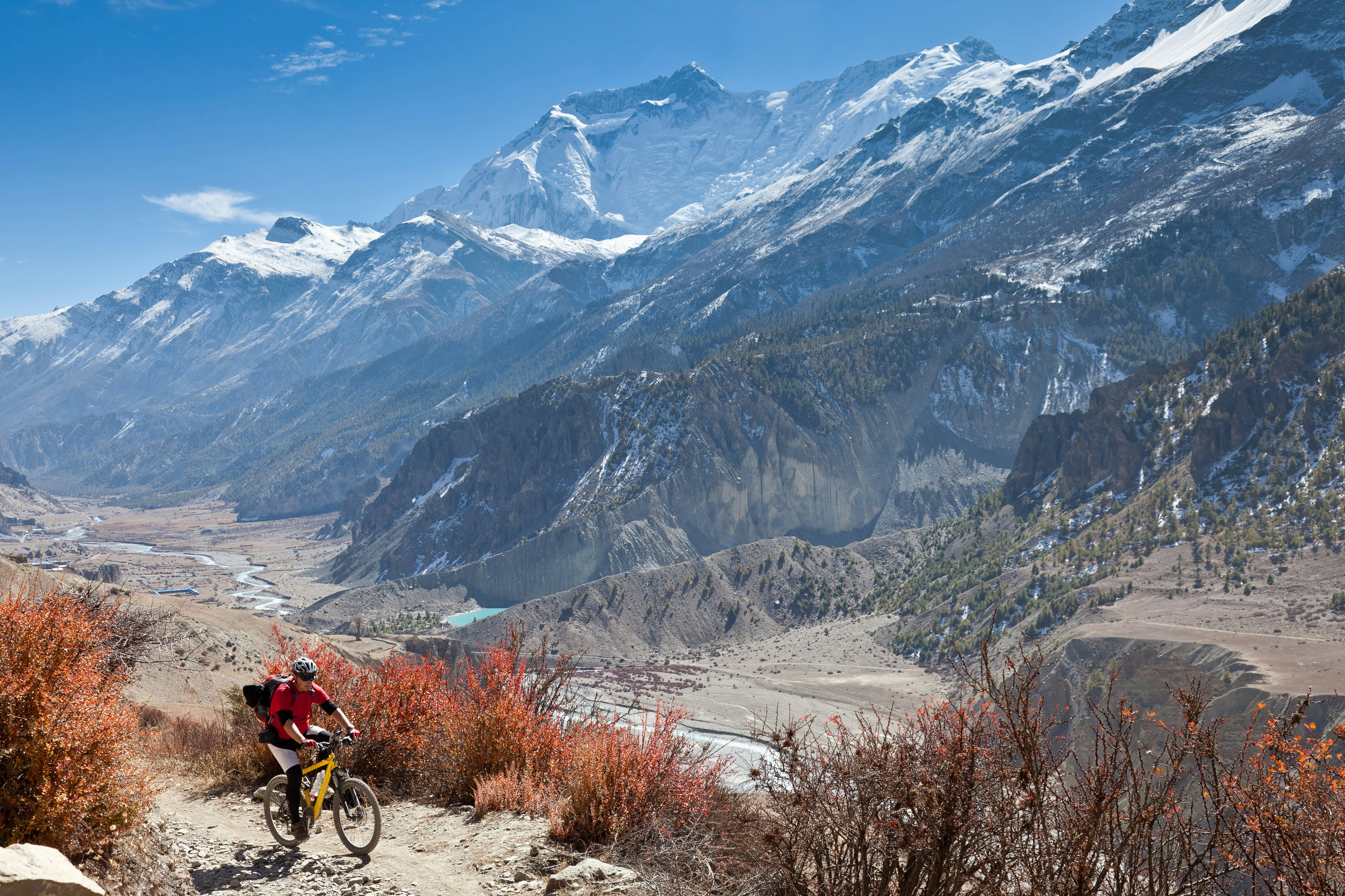 A male mountain biker has left the village of Manang and is climbing towards Thorong La in a scenery landscape on the Annapurna Circuit, Nepal. On the right side the summits of Annapurna III and Gangapurna